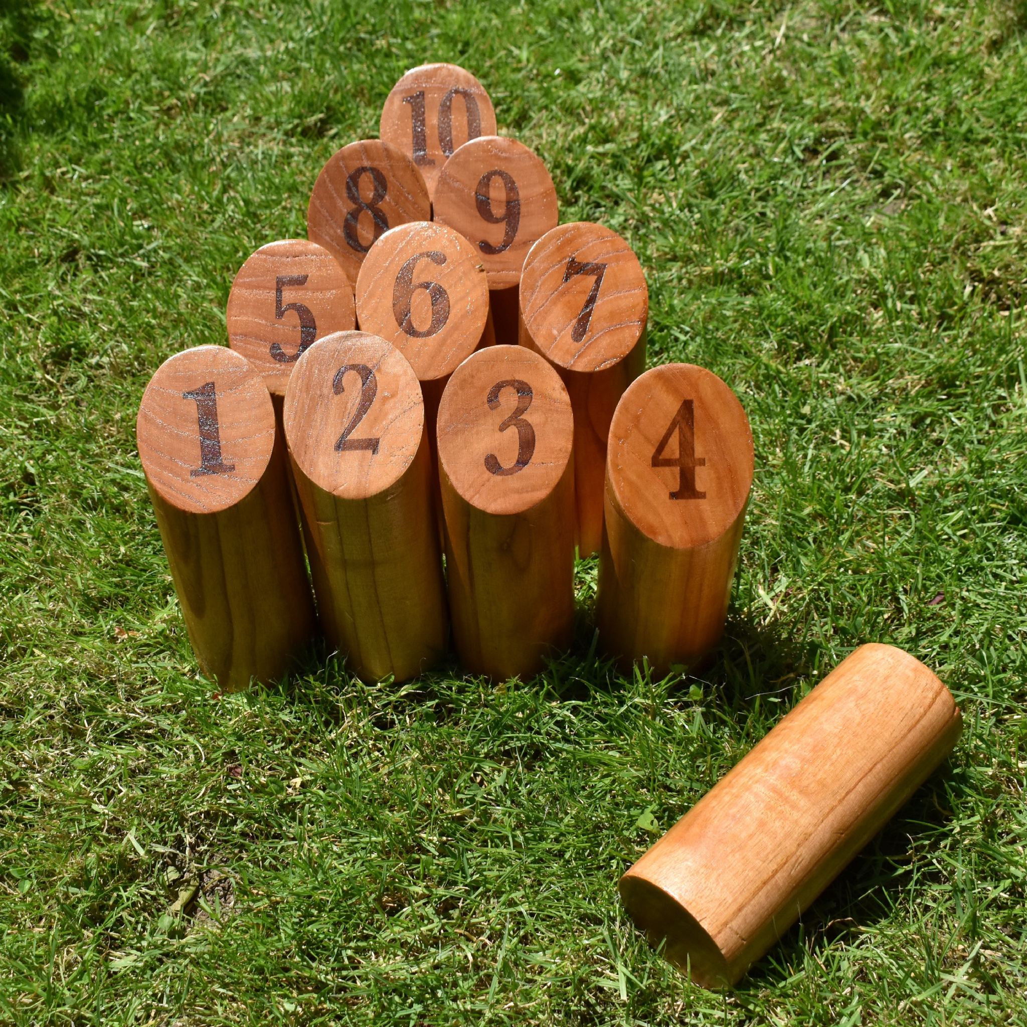 Holz-Kegelspiel auf Gras. Kegel sind mit 1-10 nummeriert. Ein Kegel liegt auf dem Gras.