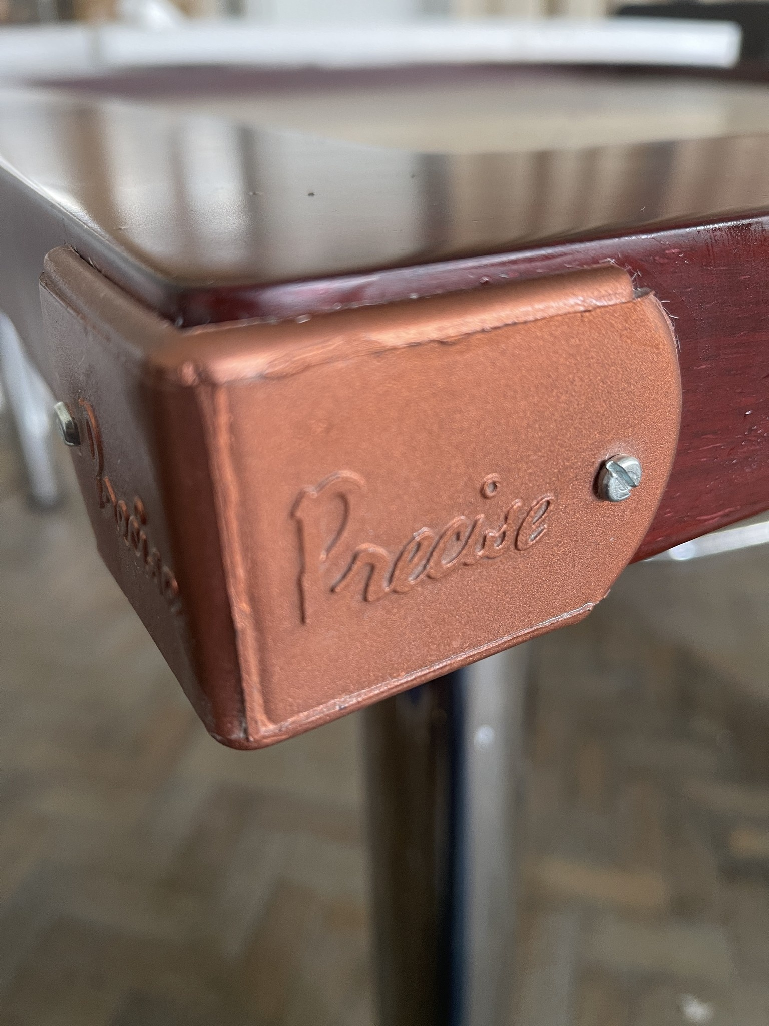 Nahaufnahme einer braunen Tischecke mit einem Metalleckenschutz mit der Aufschrift 'Precise'.