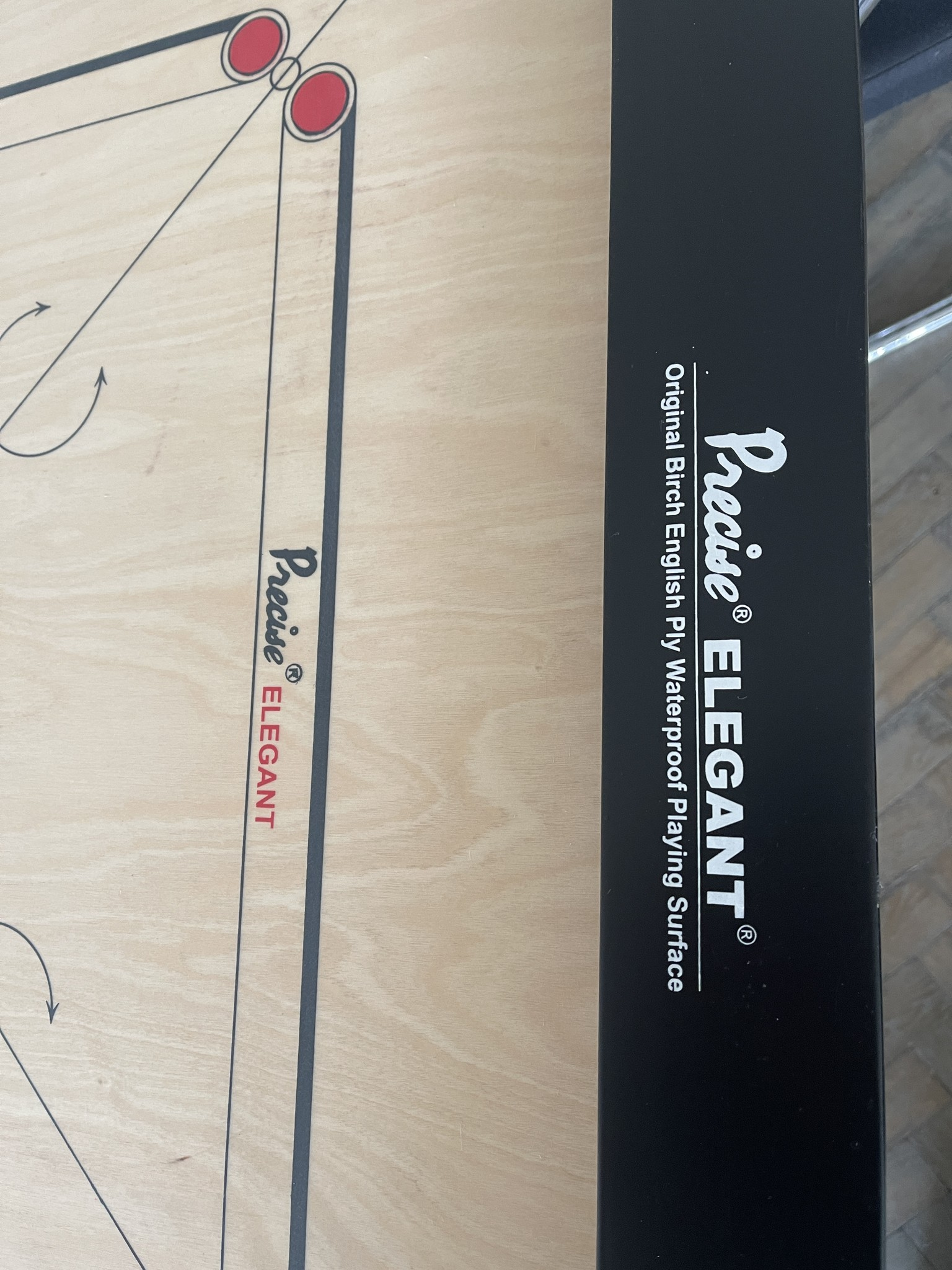 Nahaufnahme eines Carrom-Bretts. Das Brett ist hellbraun mit schwarzen Linien und roten Kreisen.
