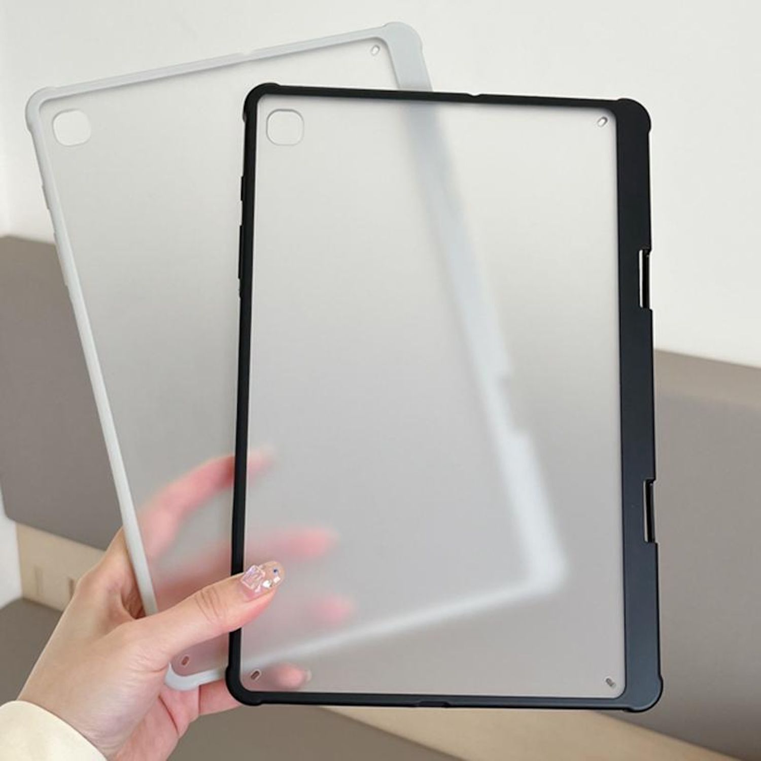Dos fundas para tabletas. Una con marco negro, otra gris claro. Una mano sostiene la funda gris.