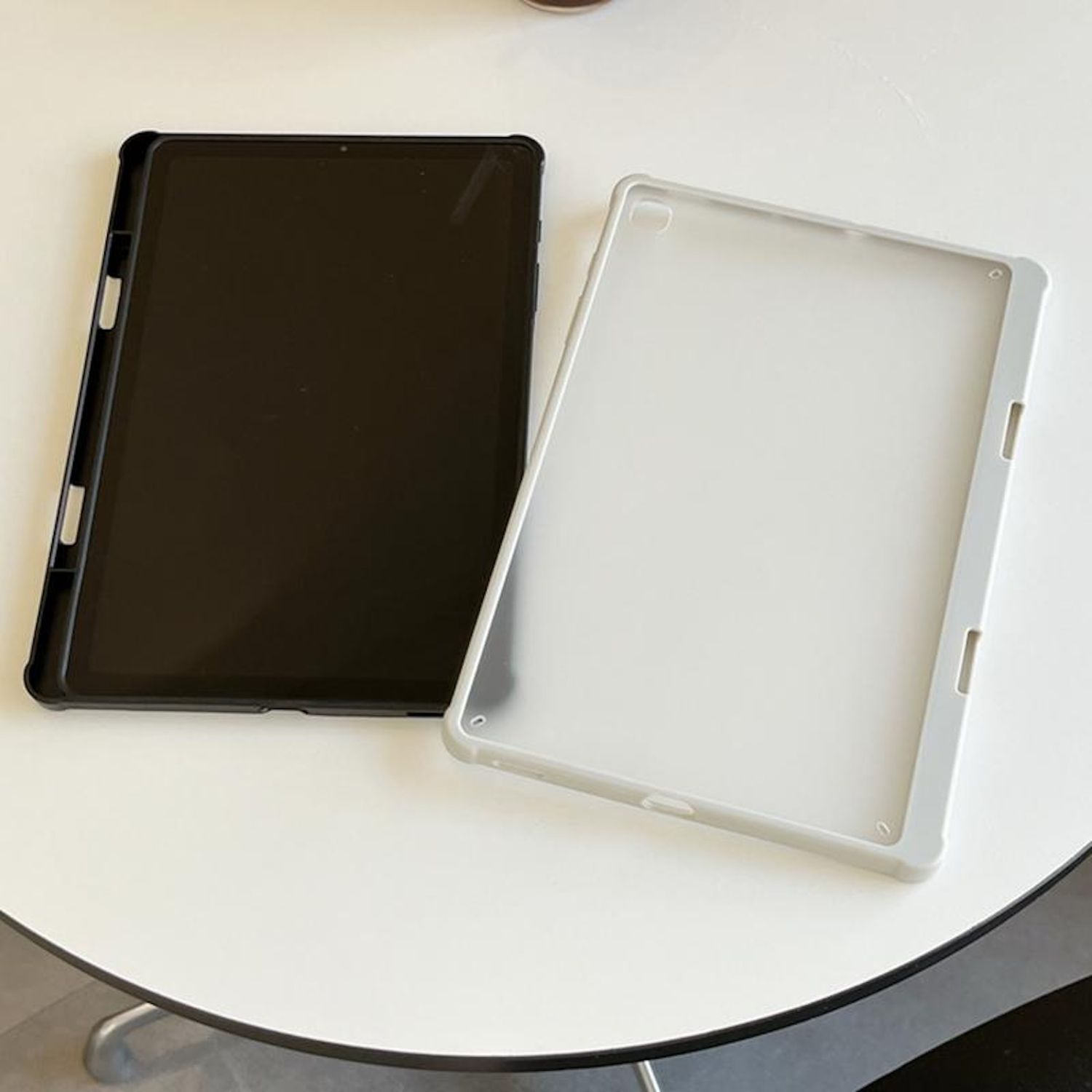 Dos fundas para tablet, una negra y otra blanca, sobre una superficie blanca.