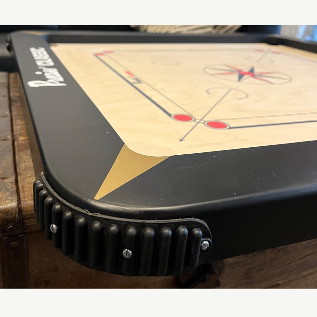 Nahaufnahme eines Carrom-Bretts. Der dunkle Rahmen hat abgerundete Ecken und goldene Details.