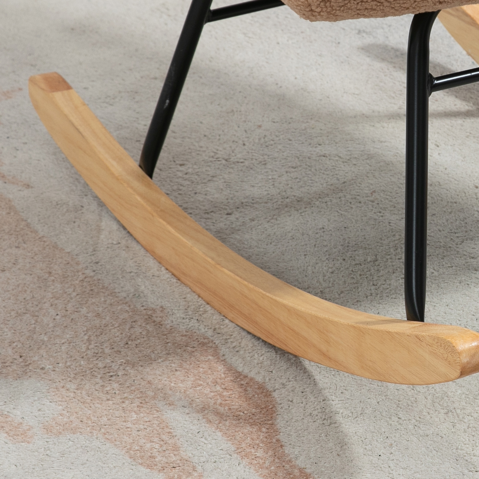 Wippsockel aus Holz mit schwarzem Metallrahmen und beigem Sitz. Auf einem gemusterten Teppich.