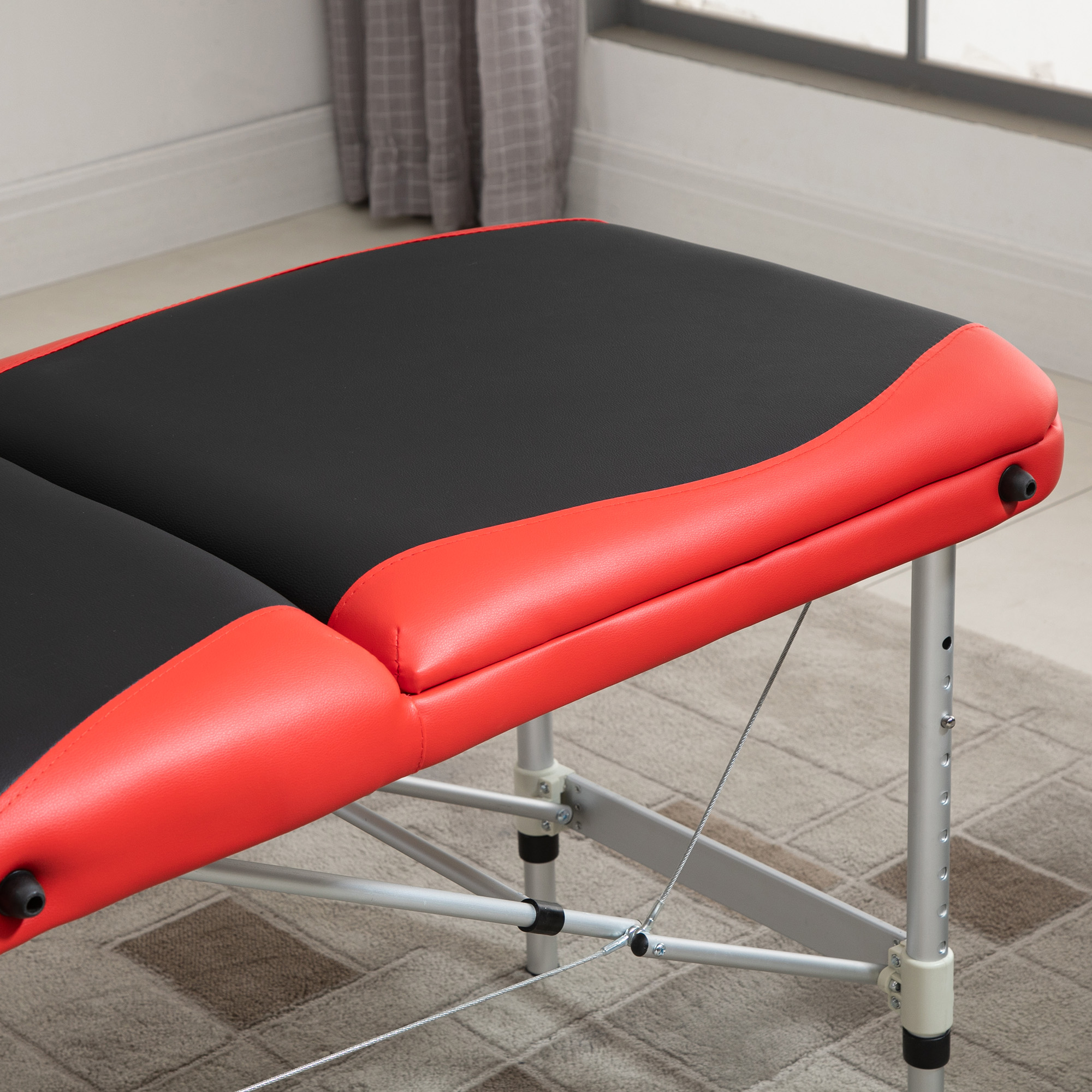 Massagetisch aufgebaut. Tisch mit roter und schwarzer Polsterung und dunkler Raum mit Fenster.