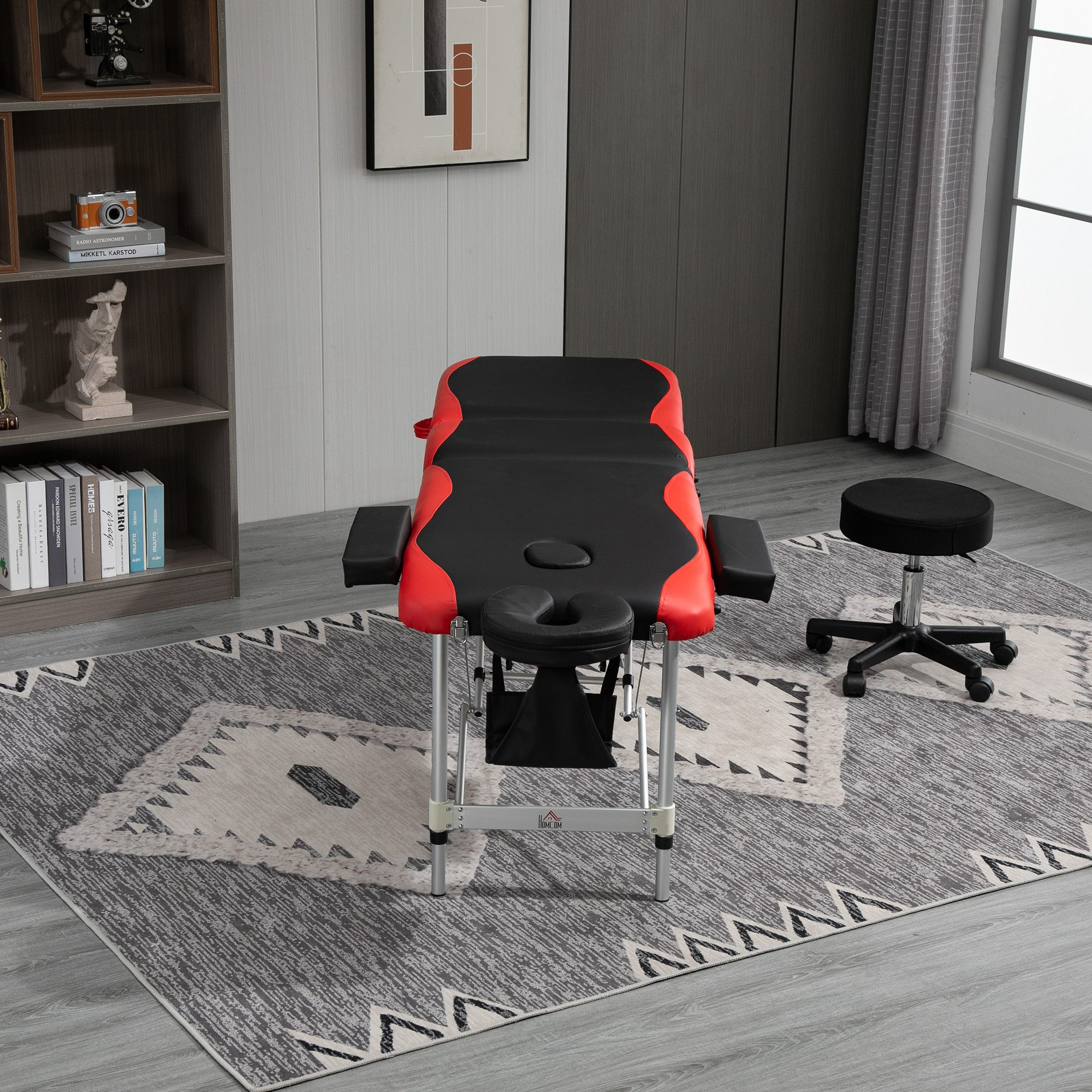 Massagetisch mit Zubehör. Enthält einen Hocker und ist in einem Raum mit gemustertem Teppich aufgestellt.