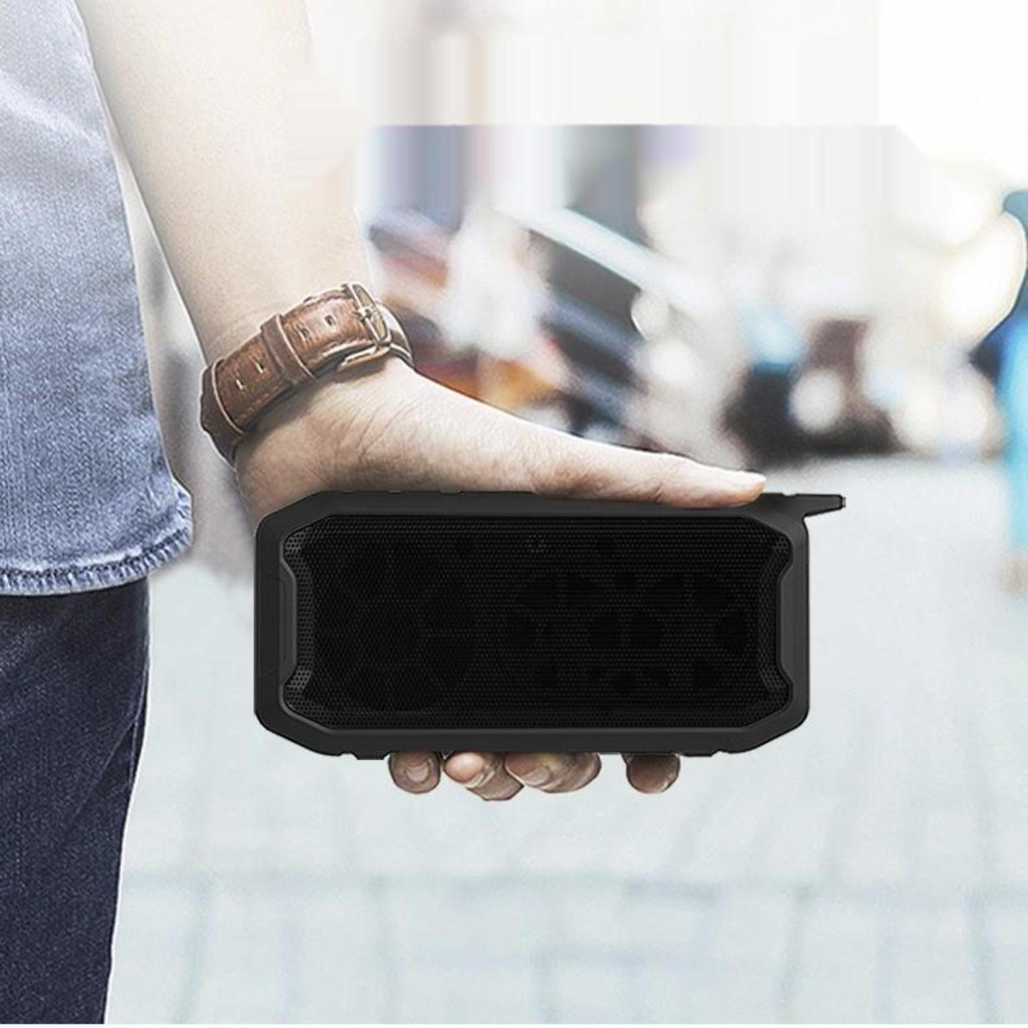Die Hand einer Person, die einen schwarzen, rechteckigen Bluetooth-Lautsprecher hält, mit einer braunen Lederuhr am Handgelenk.
