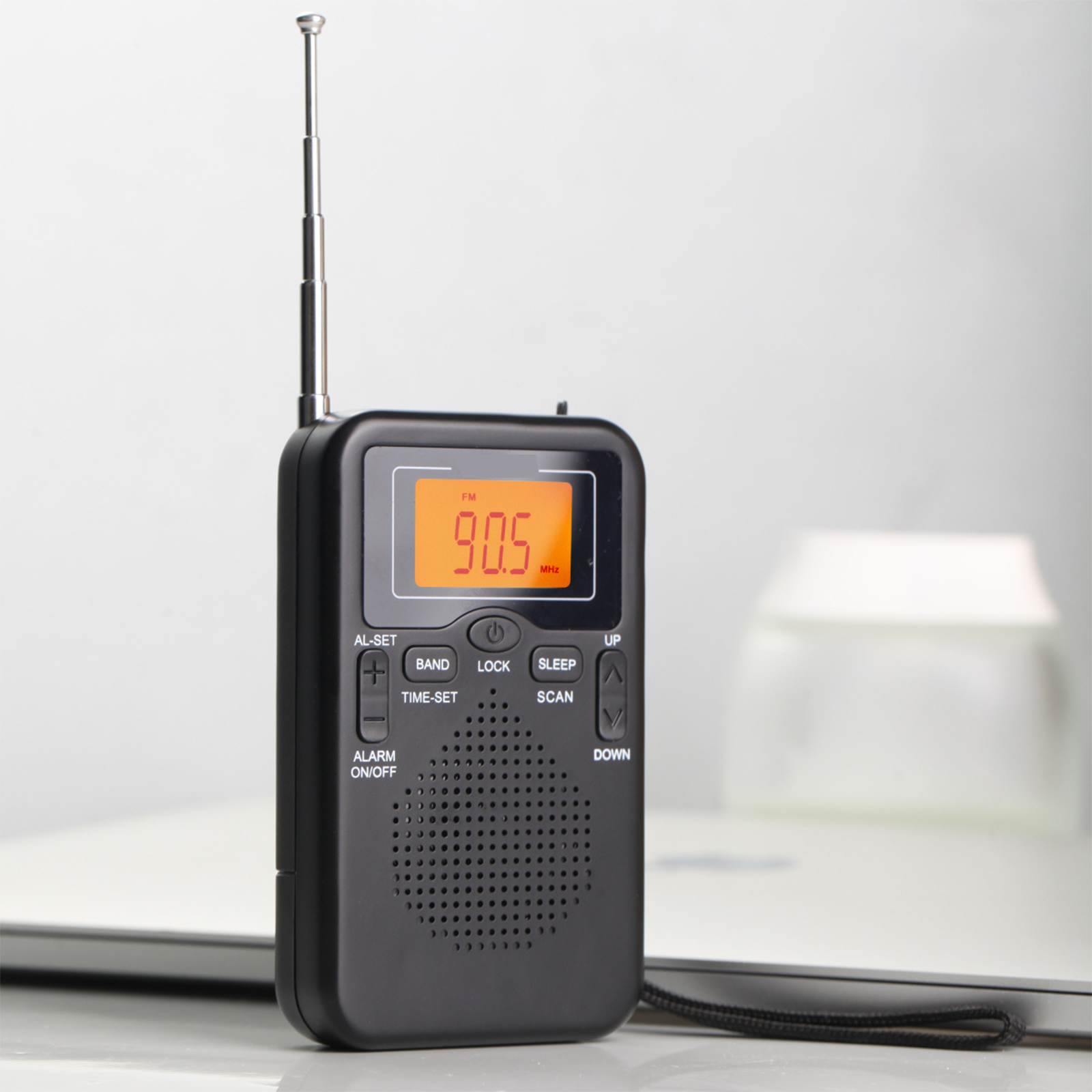 Schwarzes tragbares Radio mit orangefarbener Anzeige, die 90,5 MHz anzeigt, neben einem unscharfen Hintergrund.