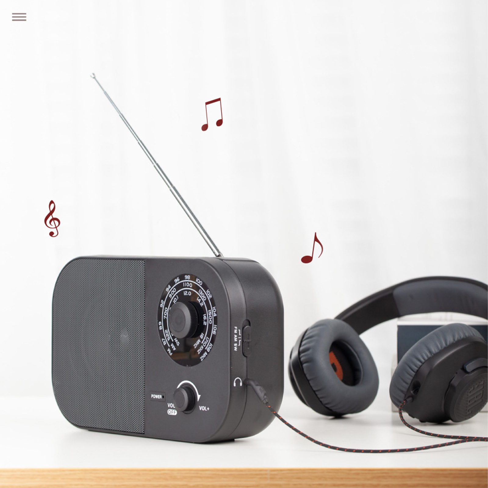 Ein schwarzes Radio, Kopfhörer und Noten auf einem Tisch. Weißer Hintergrund mit Holztischkante.