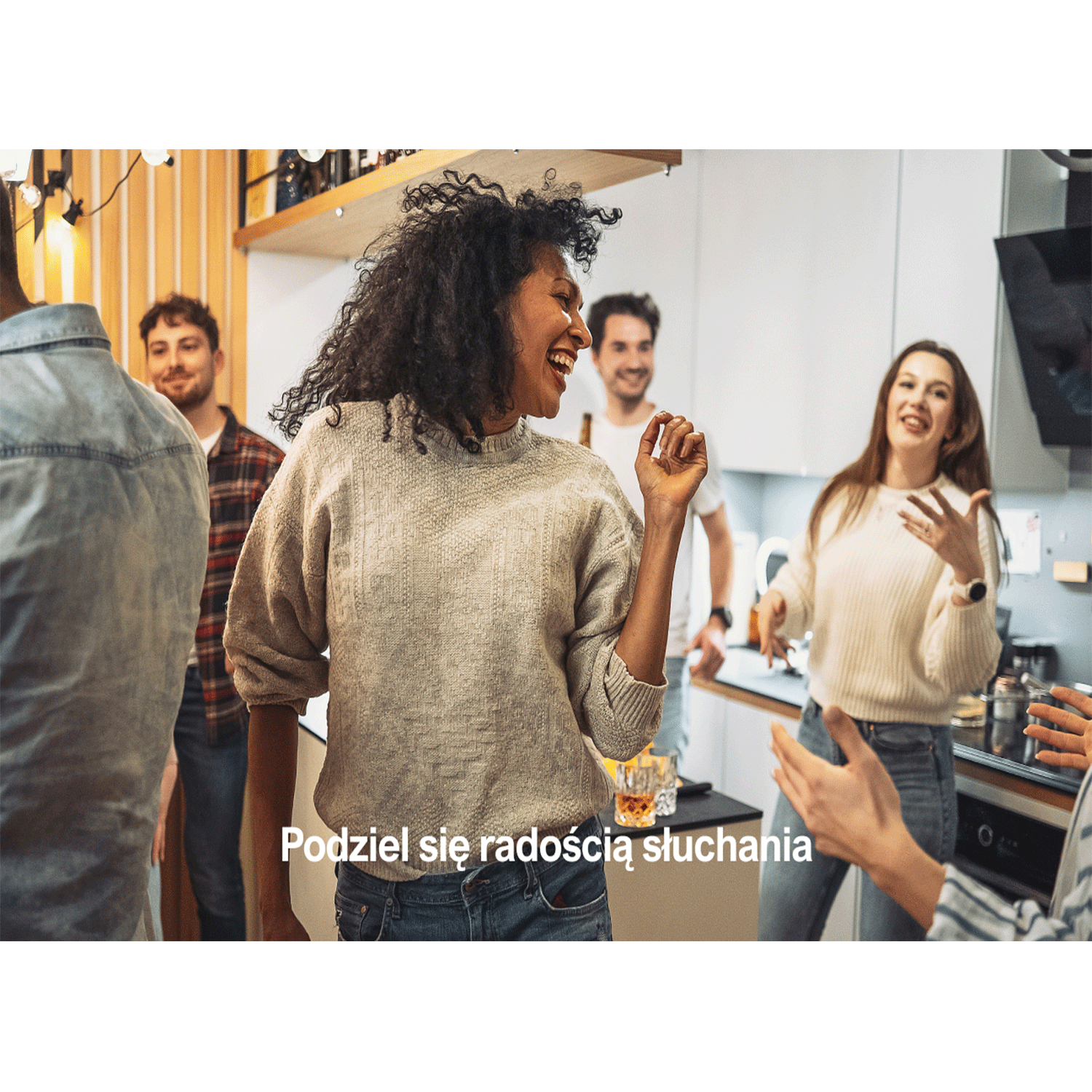 Grupa osób tańczących w kuchni, z uśmiechniętą kobietą w centrum.