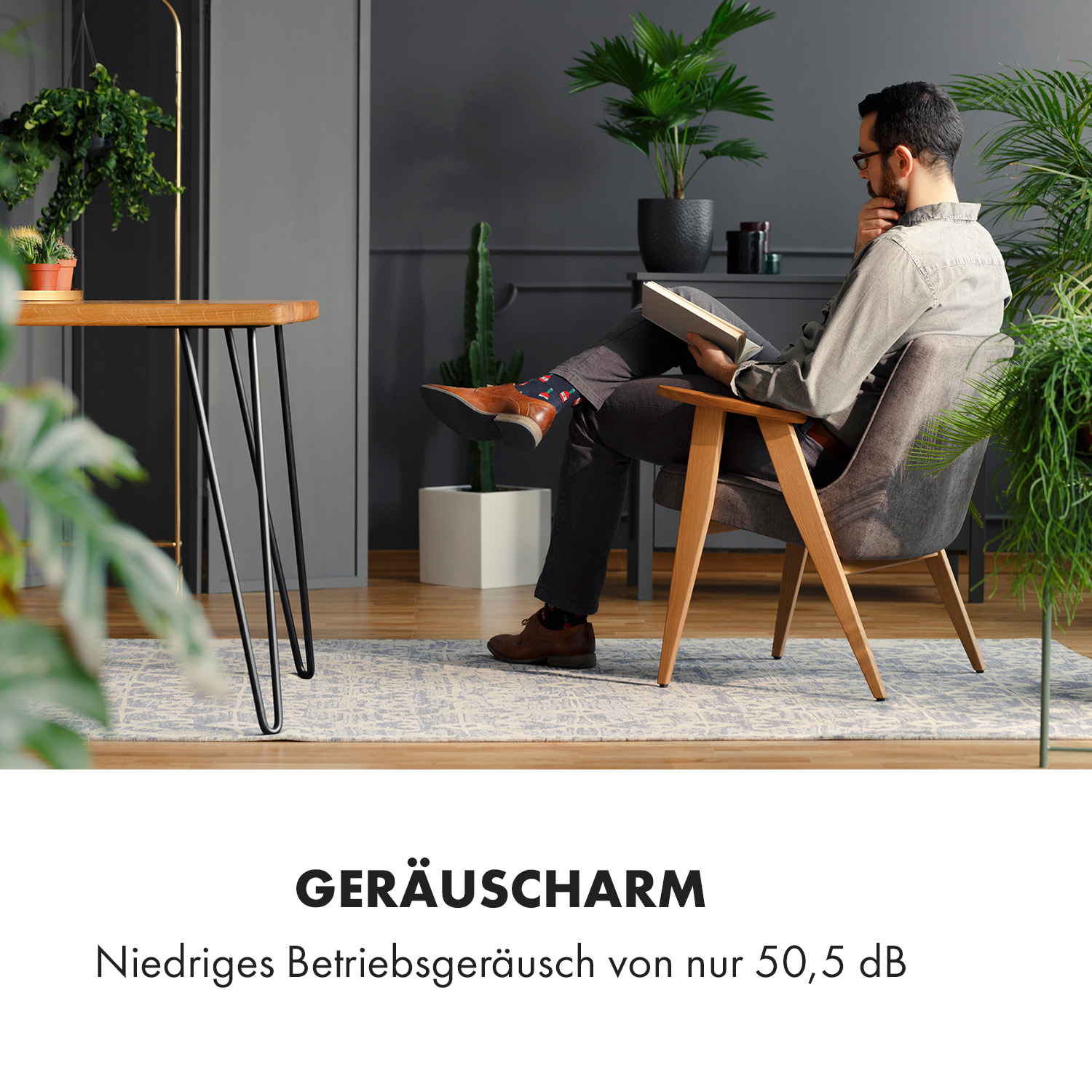 Ein Mann liest ein Buch in einem modernen Zimmer mit Pflanzen und einem Schreibtisch.