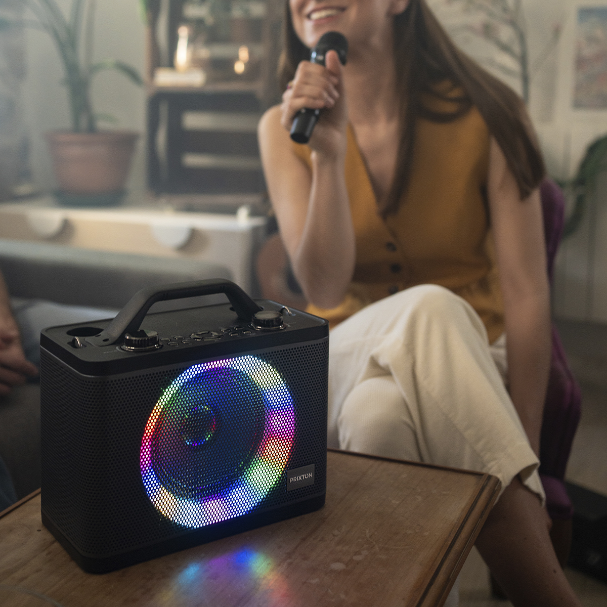 Kobieta śpiewa do mikrofonu, stojąc obok czarnego głośnika ze światłami.