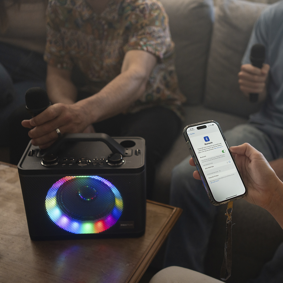 Osoba łączy się z głośnikiem Bluetooth za pomocą telefonu. Obecni są również ludzie, chipsy i stół.