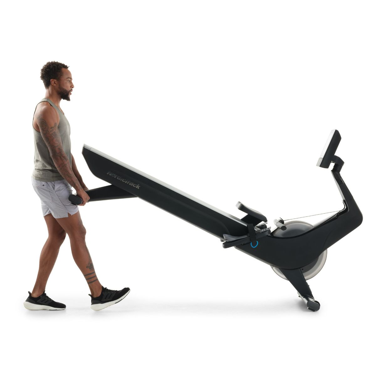 Ein Mann zieht eine schwarze Rudermaschine auf weißem Hintergrund. Er trägt ein graues Tanktop und Shorts.