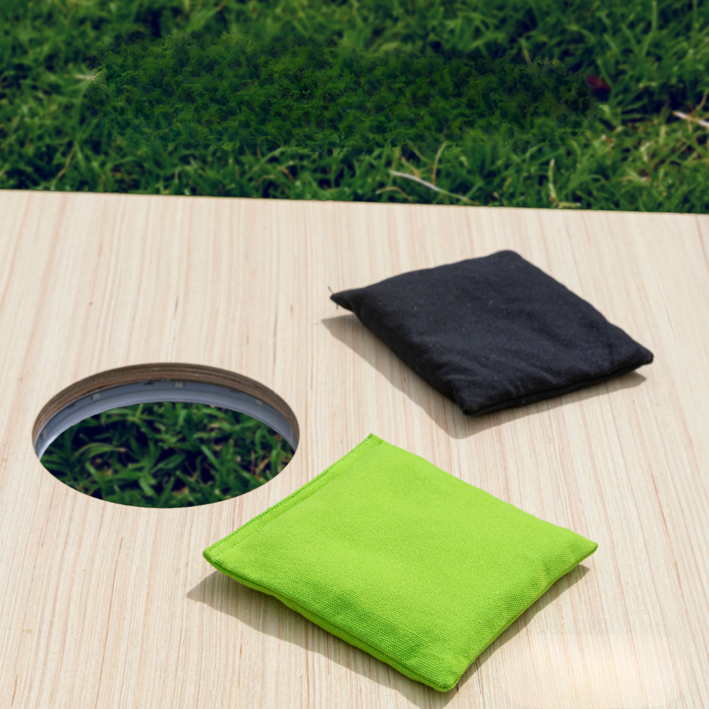 Ein Cornhole-Board aus Holz mit Loch und zwei Beanbags auf Gras.