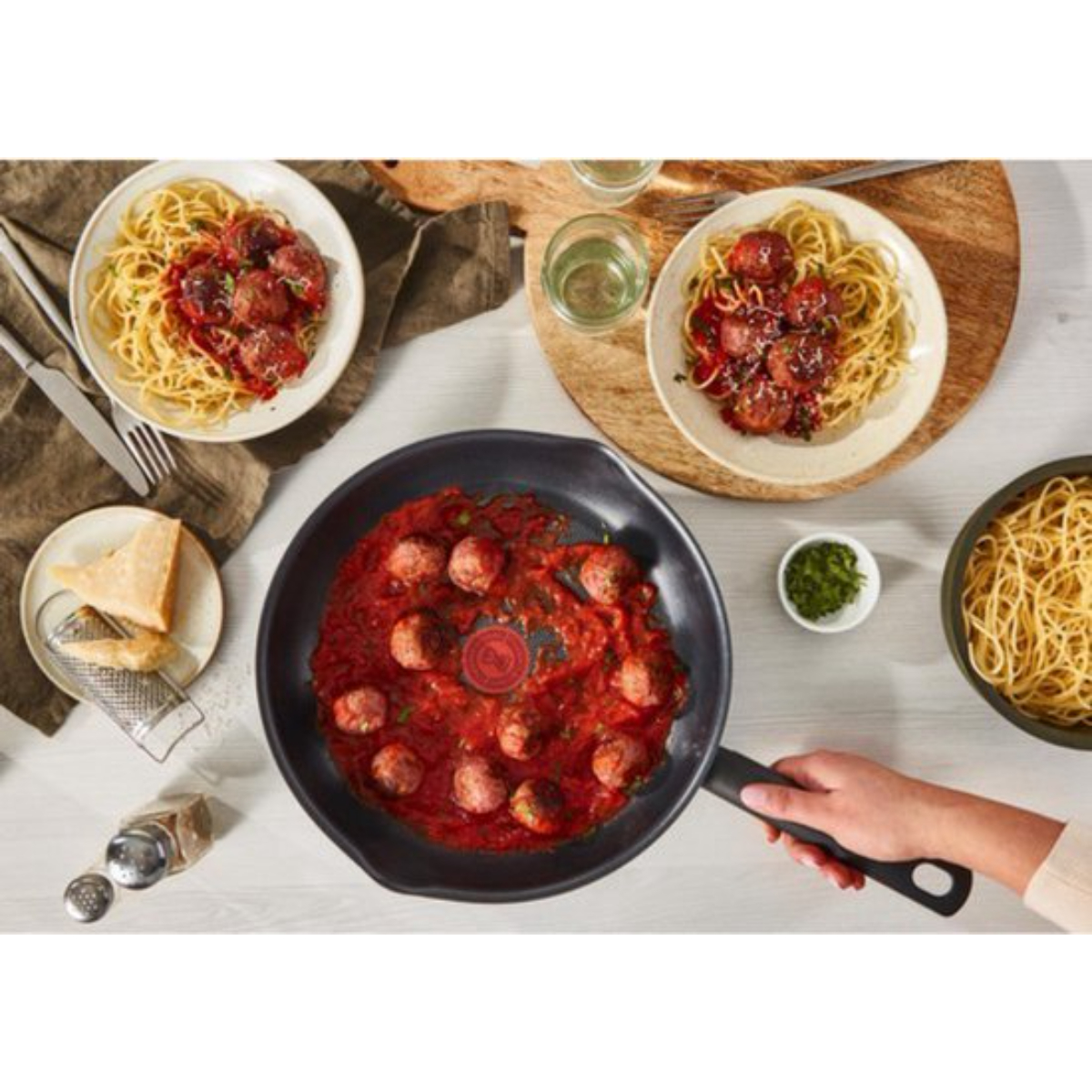 Vue aérienne d'une poêle avec des boulettes de viande et des spaghettis, avec des assiettes et des ingrédients.