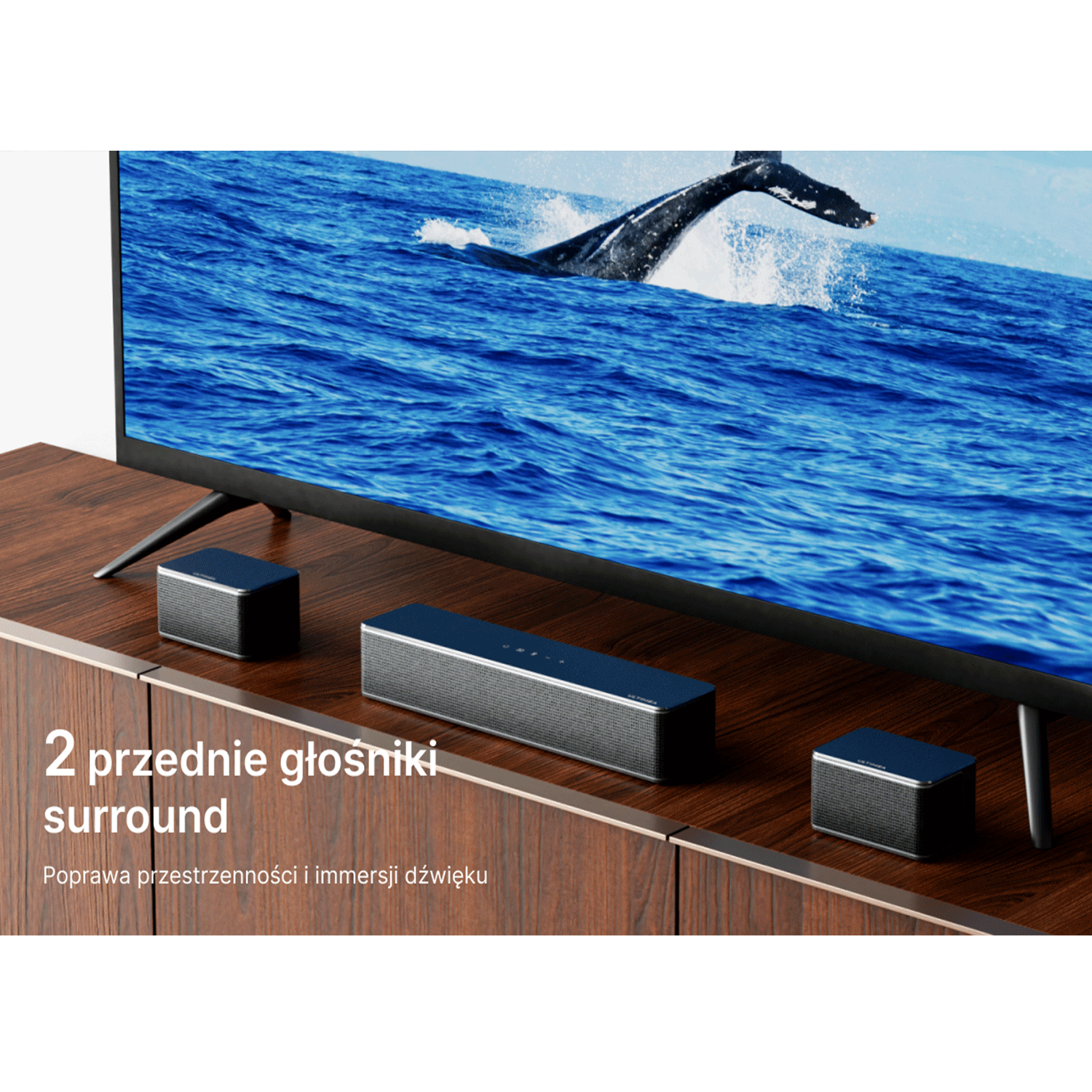 Telewizor z soundbarem i dwoma głośnikami na drewnianej szafce. Wieloryb w tle.