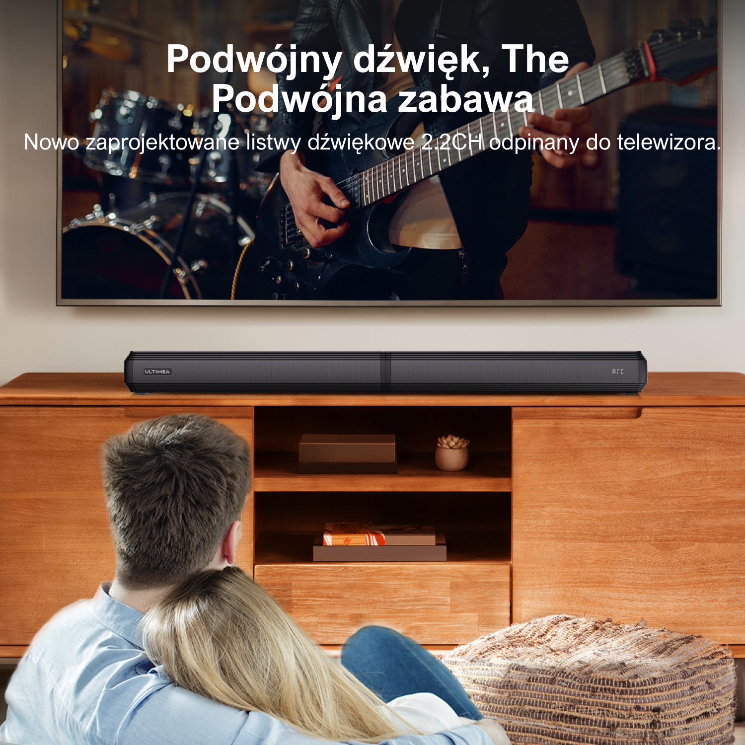 Para ogląda telewizję. Soundbar stoi na drewnianej szafce. Tekst na ekranie: 'Podwójny dźwięk, podwójna zabawa'.