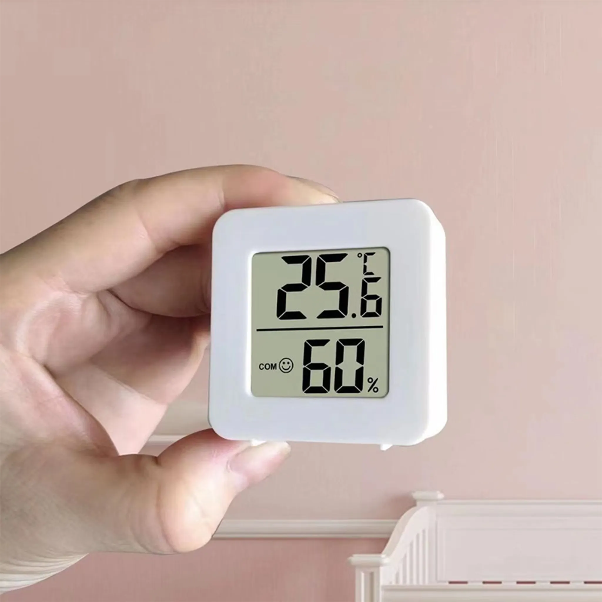 Hand, die eine weiße Digitalanzeige mit 25,6 °C Temperatur und 60 % Luftfeuchtigkeit hält.