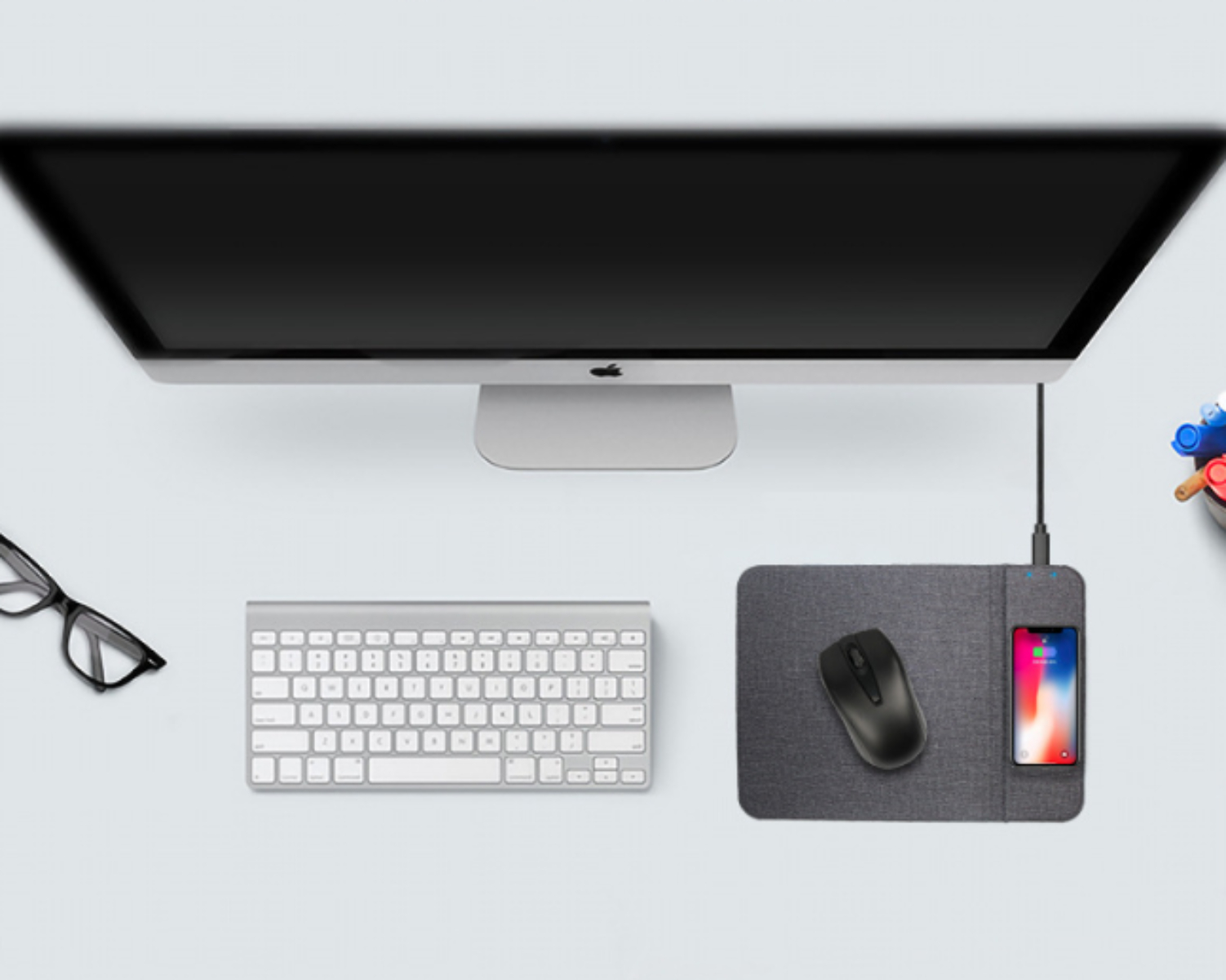 Draufsicht auf einen Computeraufbau. Enthält einen Monitor, eine Tastatur, eine Maus, ein Telefon auf einem Ladepad und eine Brille.