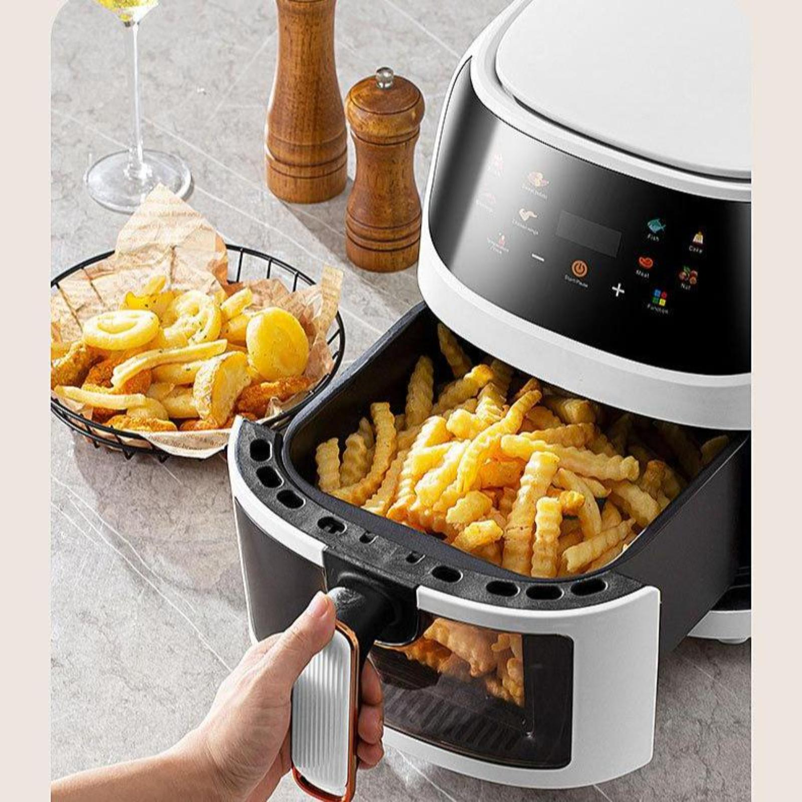 Weiße Heißluftfritteuse mit Pommes Frites im Inneren. Eine Person hält den Griff. Ein Glas Wein und Holzschüttler daneben.