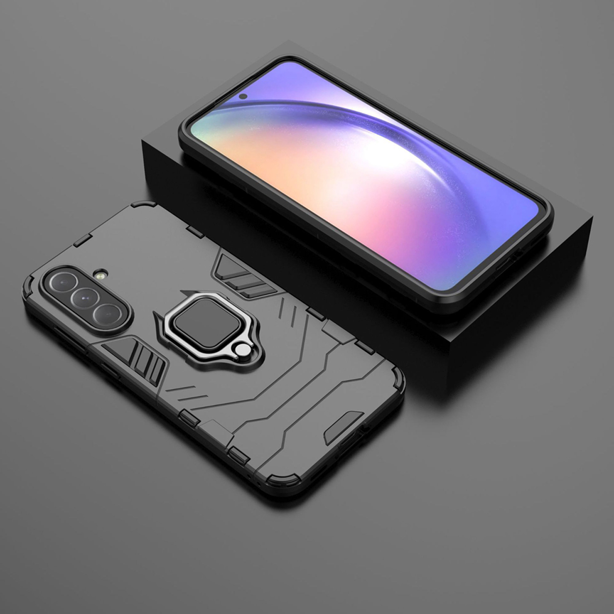 Een telefoon met een zwart hoesje op een zwart oppervlak. De hoes heeft een ringhouder. Een ander hoesje staat in de buurt.