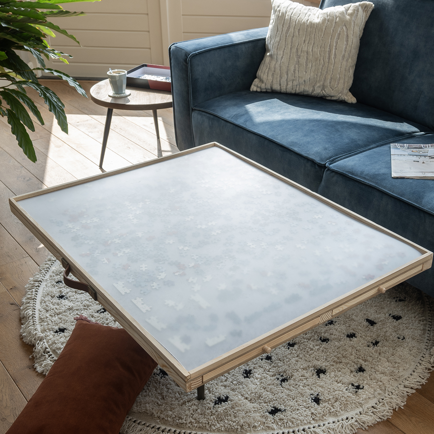 A wooden framed puzzle table with a completed puzzle. Sofa, rug, and side table in the background.