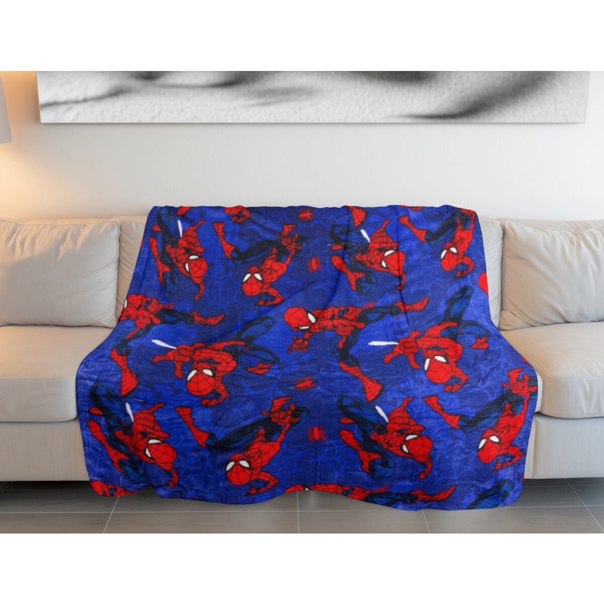 Blaue Decke mit vielen Spider-Man-Figuren auf einem weißen Sofa vor einer Wand.