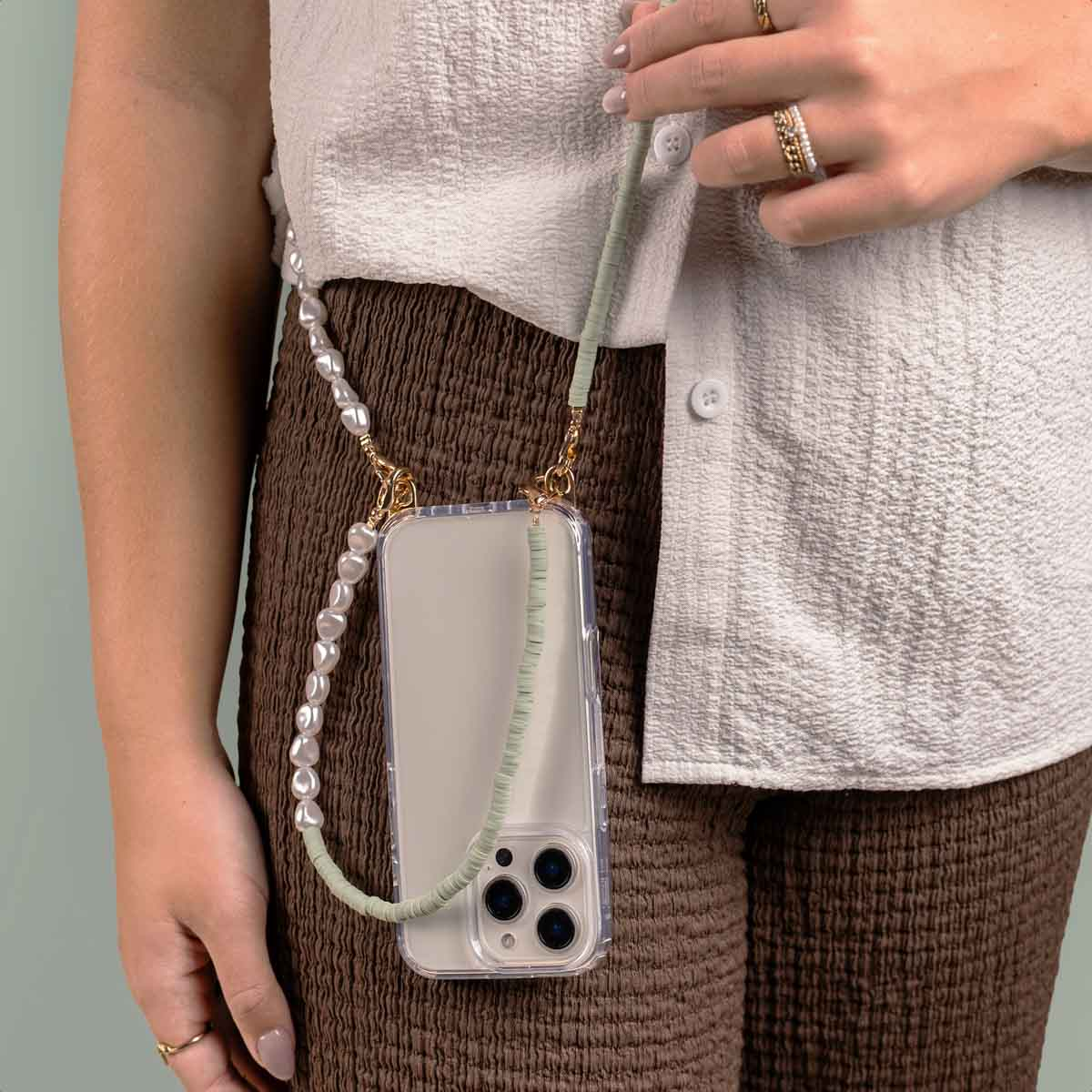 Una persona tiene in mano un telefono con un cinturino a collana di perle. Il telefono è in una custodia.