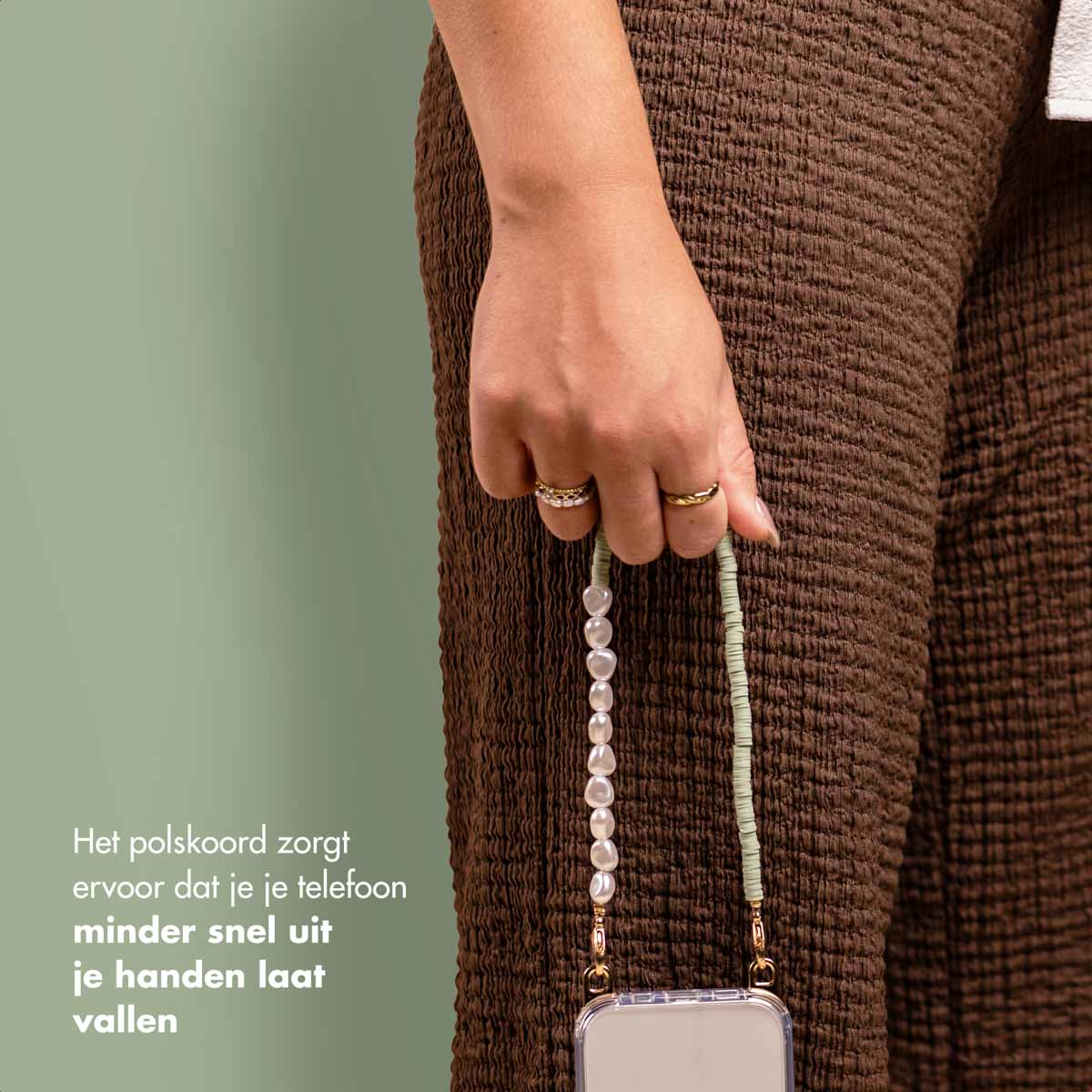 Persona che tiene in mano un telefono con un cinturino a collana di perle, accanto a pantaloni marroni. Anelli sulla mano.