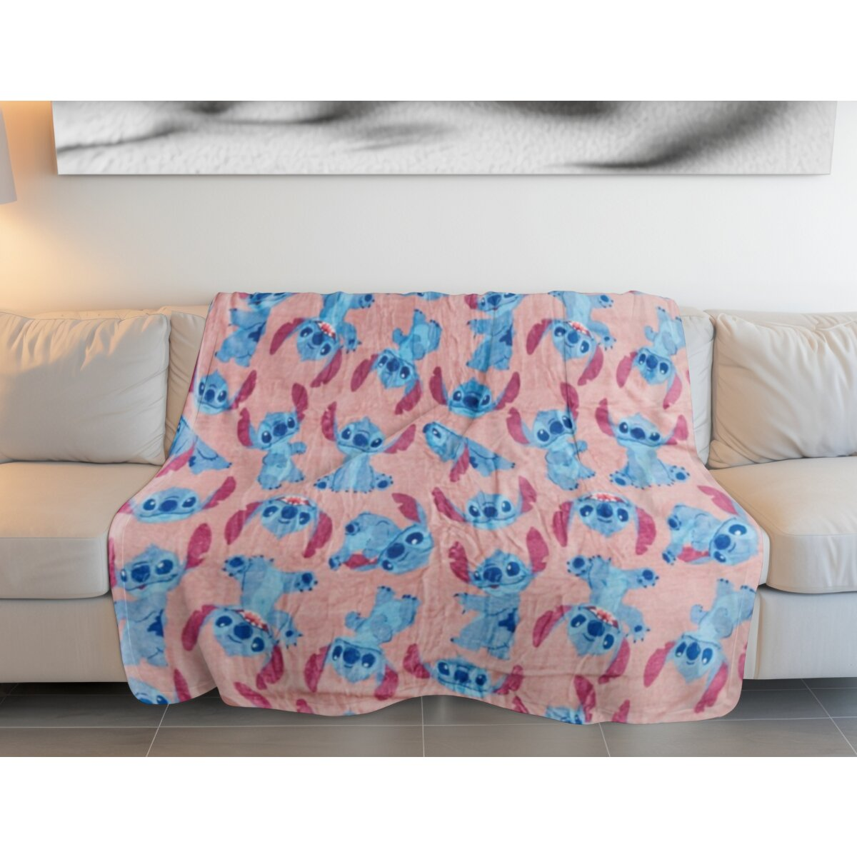 Rosa Decke auf weißem Sofa mit blauen Stitch-Cartoonfiguren. Weiße Wand im Hintergrund.