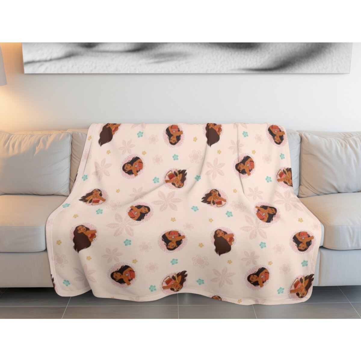 Eine hellrosa Decke mit sich wiederholenden Gesichtern von Cartoon-Mädchen, Blumen und Sternen. Die Decke liegt auf einem Sofa.