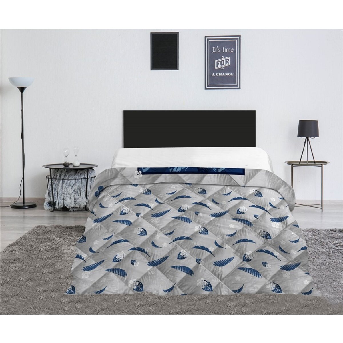 Ein Bett mit grauer Steppdecke mit blauen Blättern. Schwarzes Kopfteil und Wandkunst.