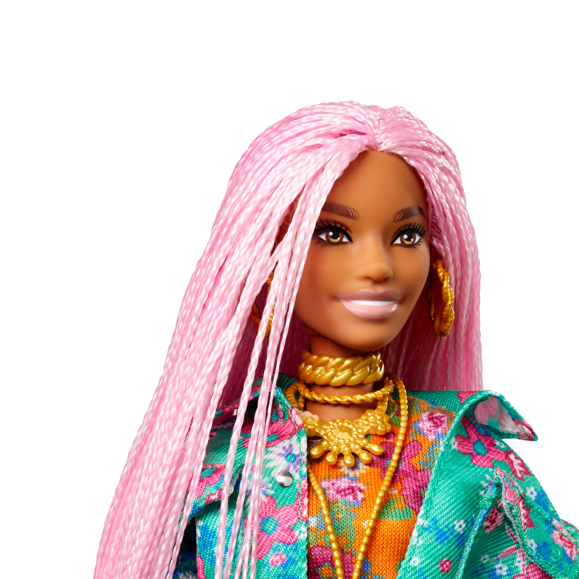 Nahaufnahme einer Barbie-Puppe mit rosa Zöpfen, Goldschmuck und Blumenjacke. Sie lächelt.