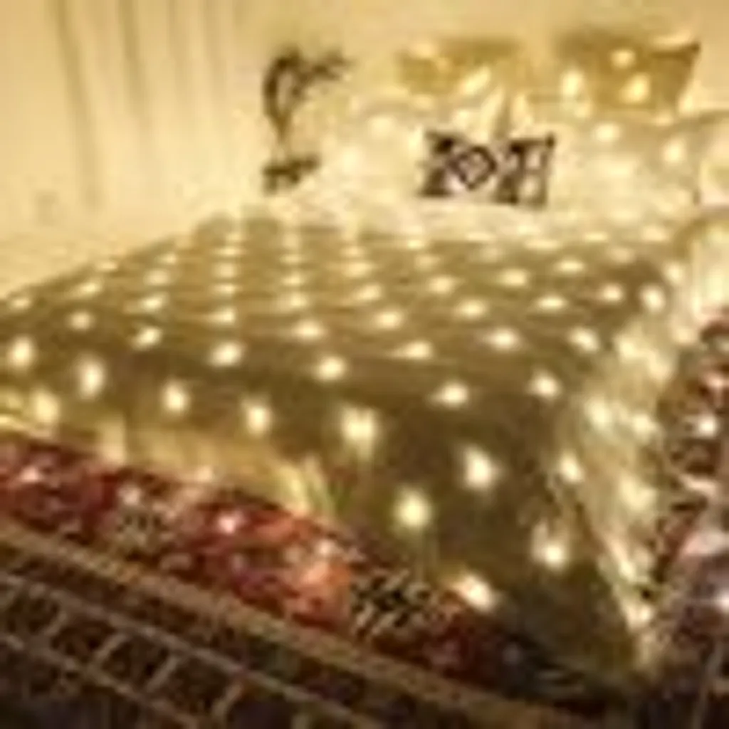 Ein Bett mit weißen Kissen und einer mit Lichtern bedeckten Decke. Darunter ein gemusterter Teppich.