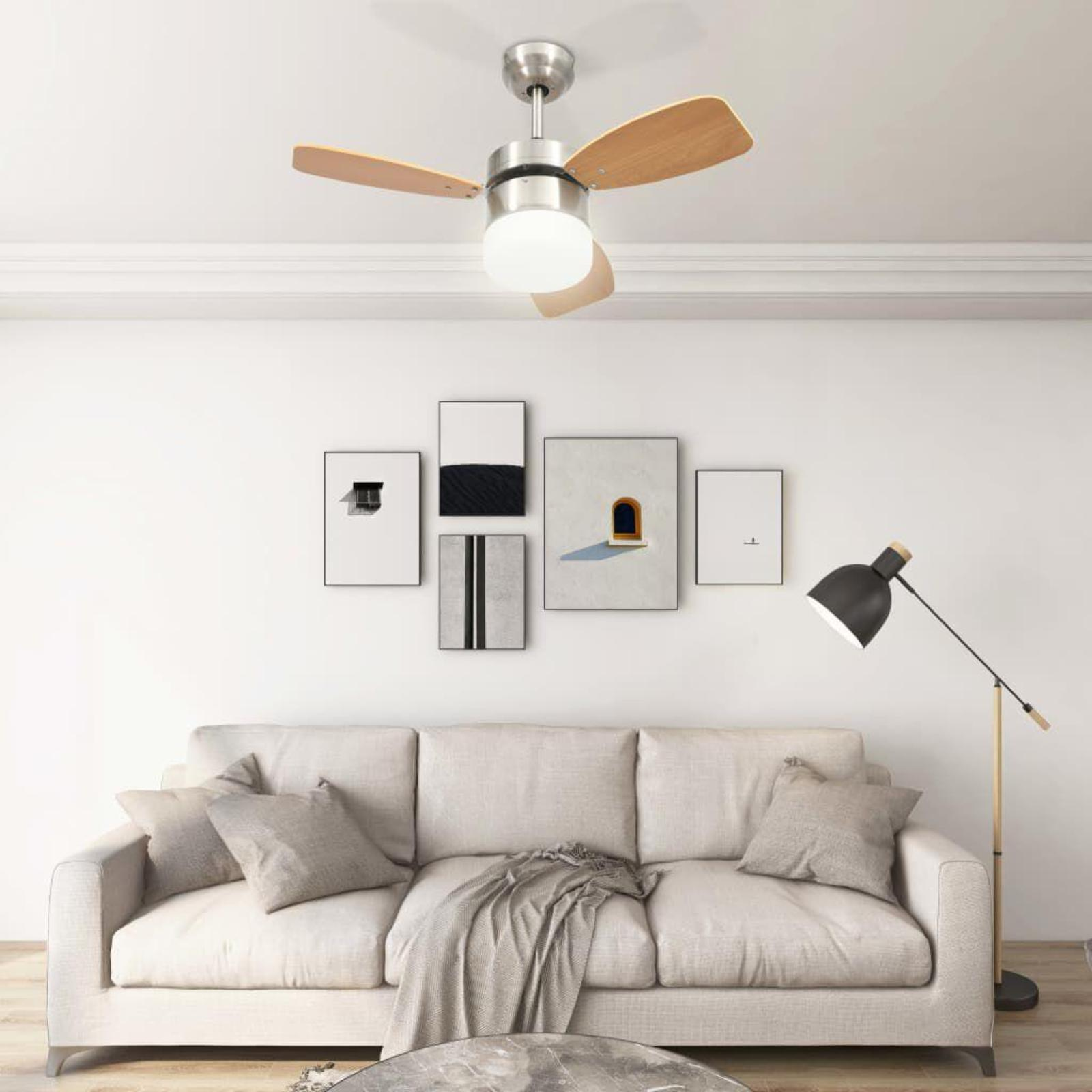 Deckenventilator mit Holzflügeln. Fünf gerahmte Bilder an der Wand, eine Couch und eine Stehlampe.