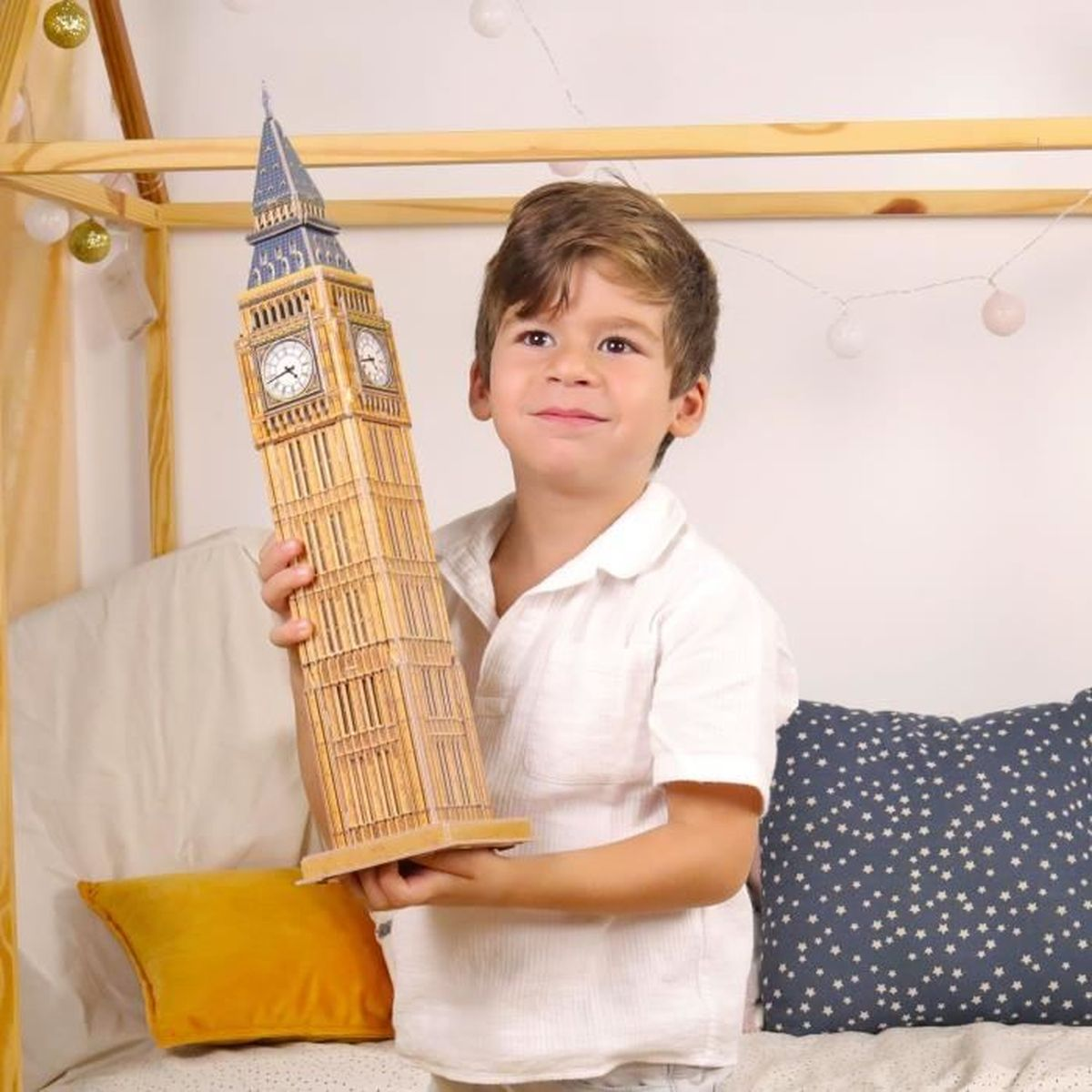 Un ragazzino tiene in mano un modello del Big Ben. Il modello della torre dell'orologio è beige e blu. Sorride.