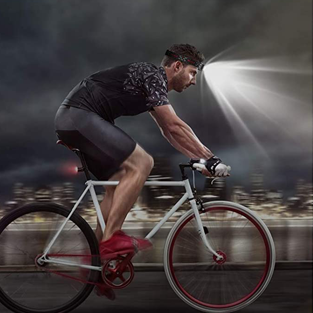 Ein Radfahrer bei Nacht mit einer Stirnlampe auf einem weißen Fahrrad. Stadtlichter im Hintergrund.