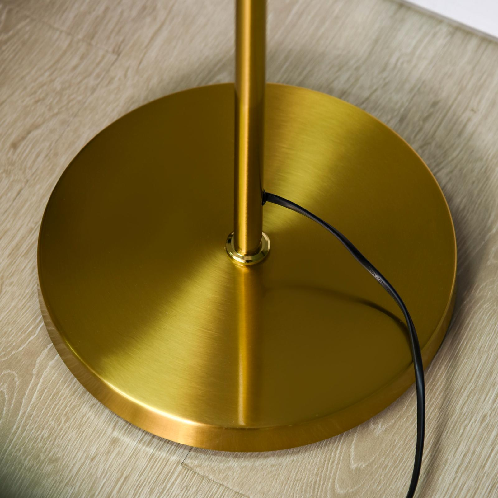 Goldener Stehlampenfuß mit schwarzem Netzkabel auf Holzboden. Die Lampe ist golden.