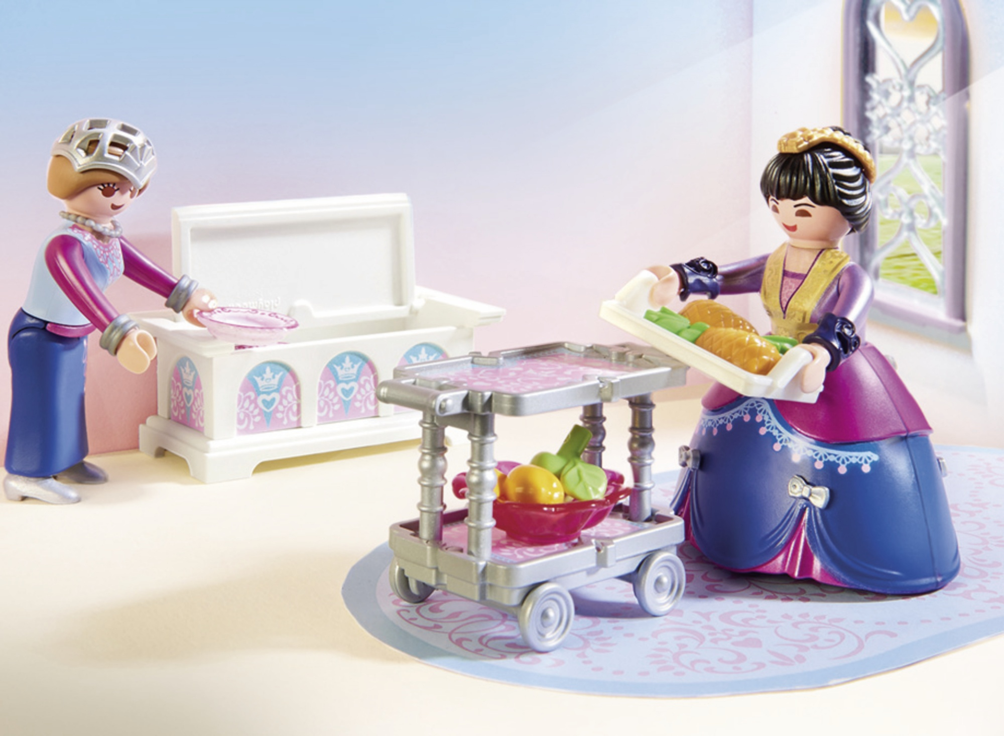 Dos figuras Playmobil con mesa blanca y carrito de servicio con comida. Fondo con ventana.