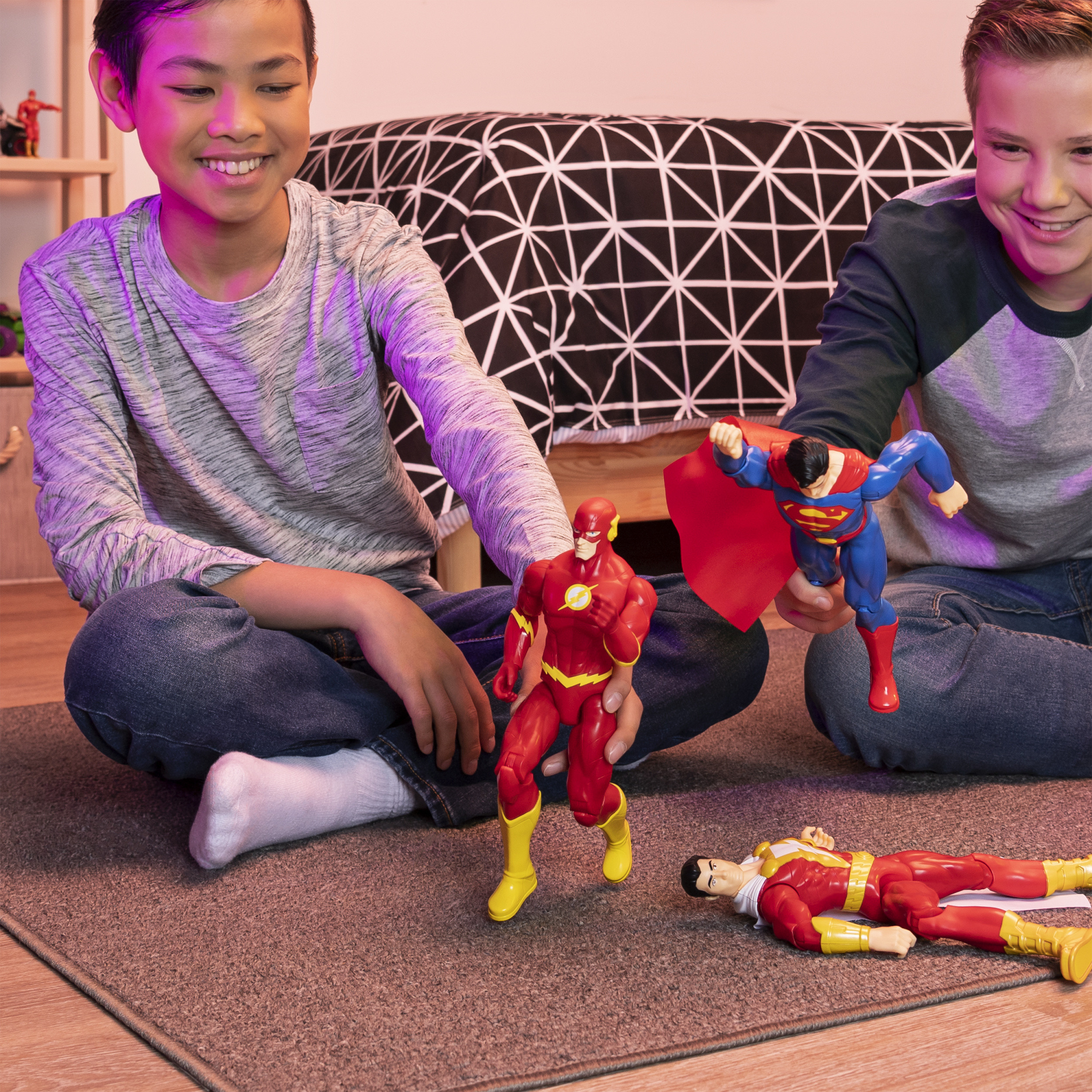 Dwóch chłopców bawi się figurkami superbohaterów. Flash stoi, Superman leci, Shazam leży.