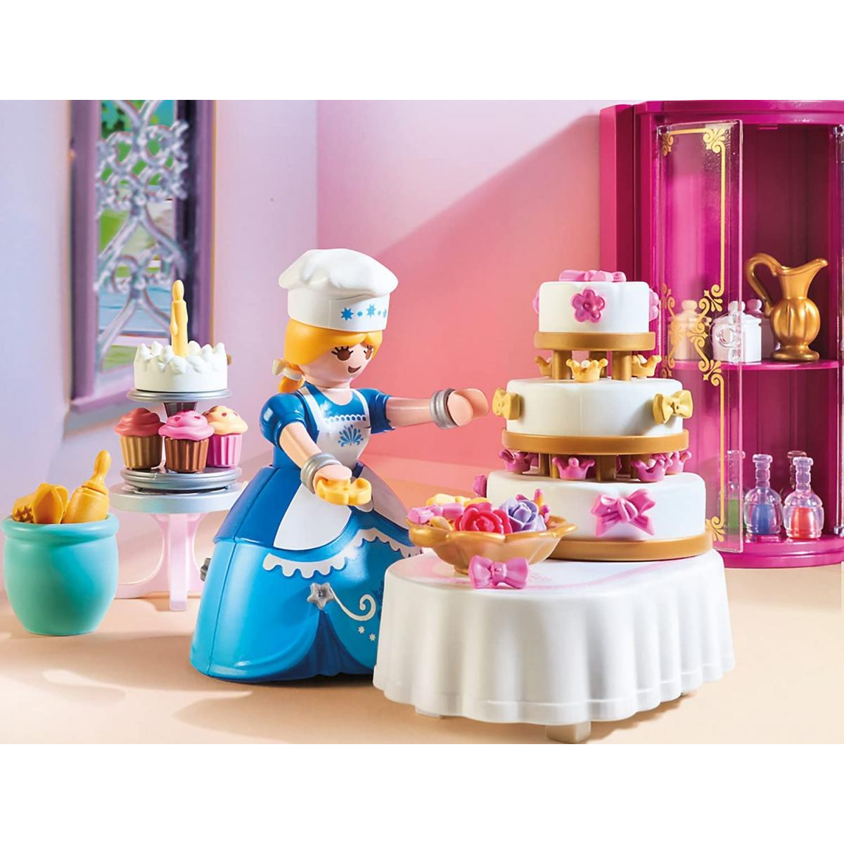 Un chef de juguete decora un pastel grande, con cupcakes y otros pasteles al fondo.