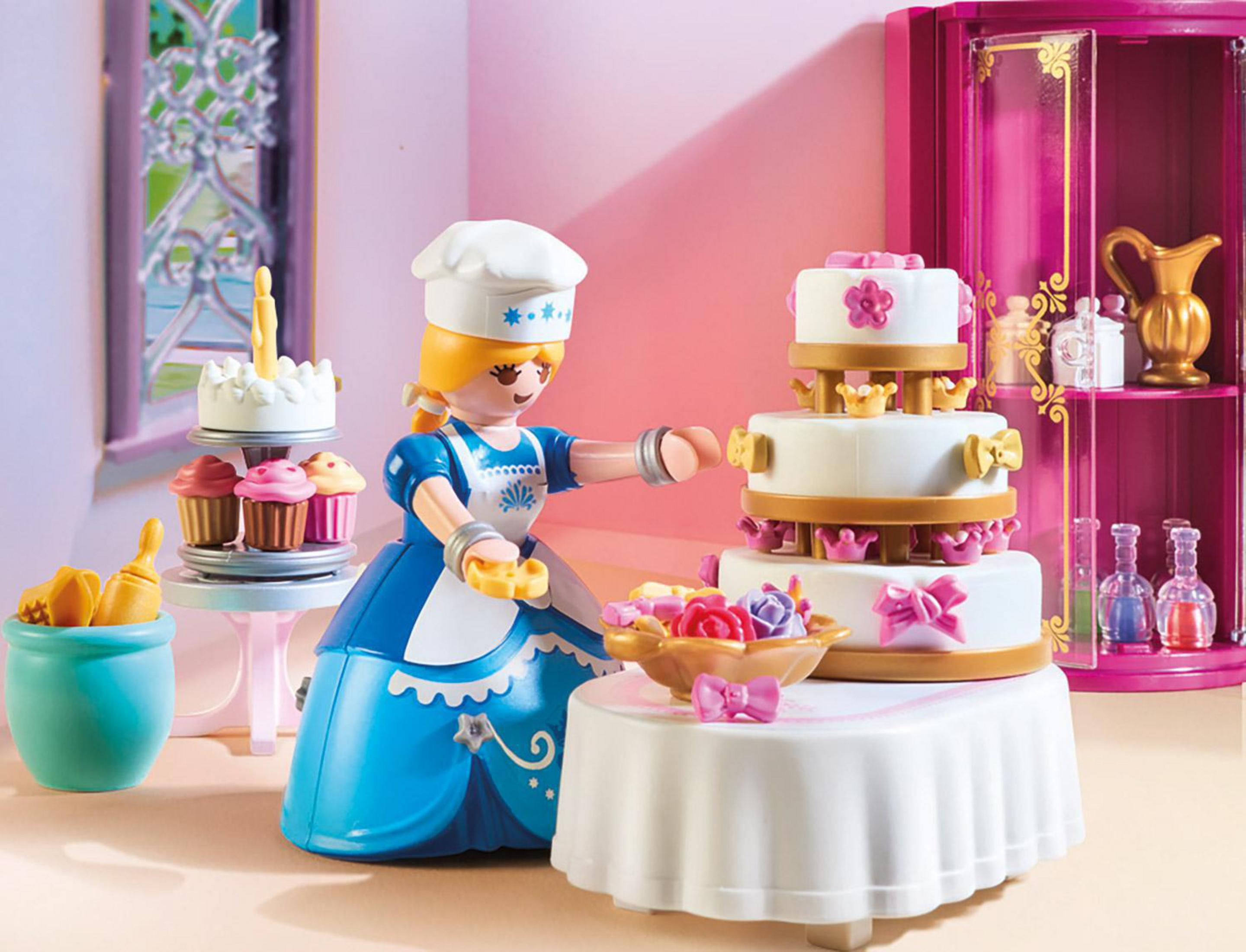 Un chef de juguete decora un pastel de tres niveles con cupcakes y otros pasteles cerca.