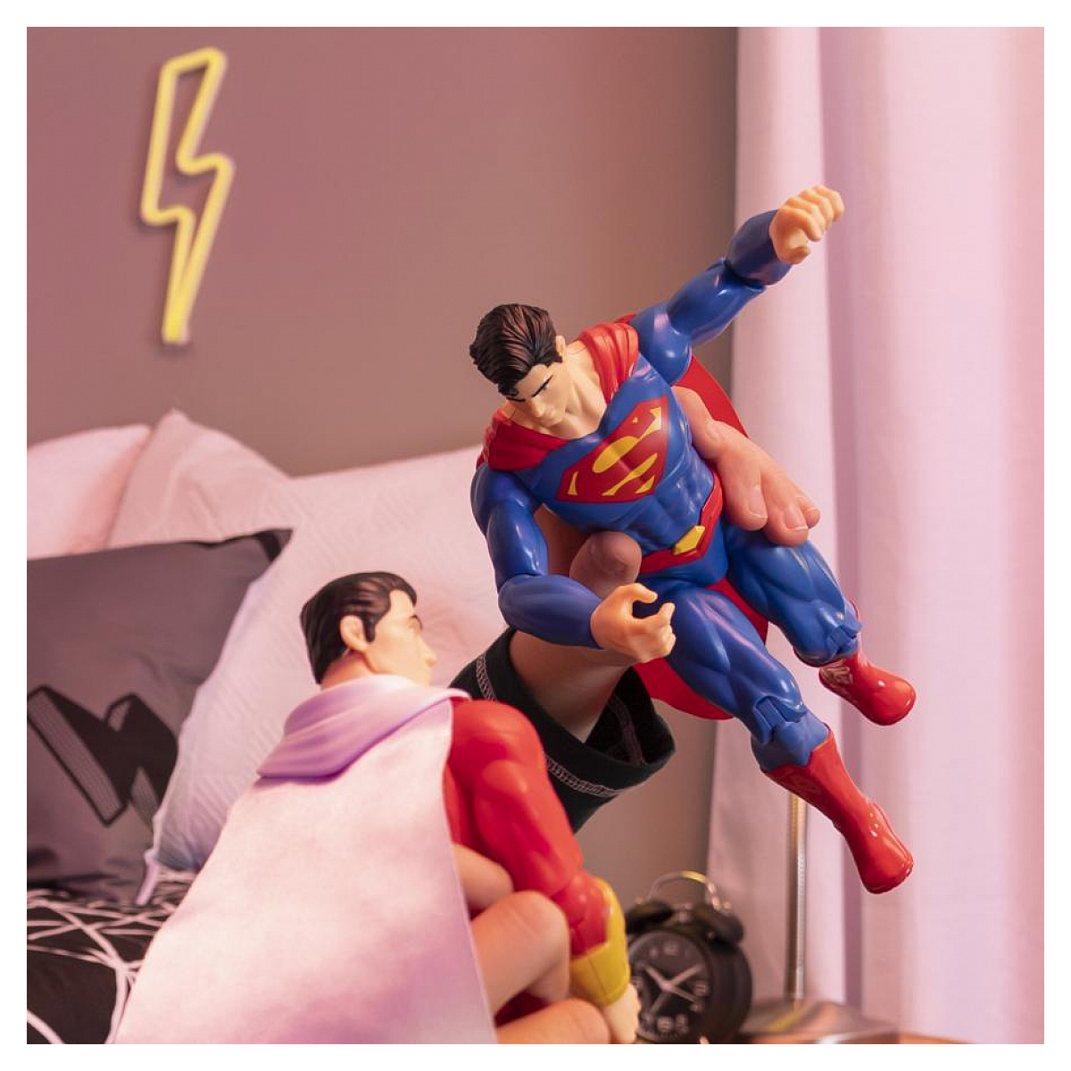 Figurka Supermana w powietrzu. Inna figurka ją trzyma. Sypialnia z dekoracją w kształcie błyskawicy.