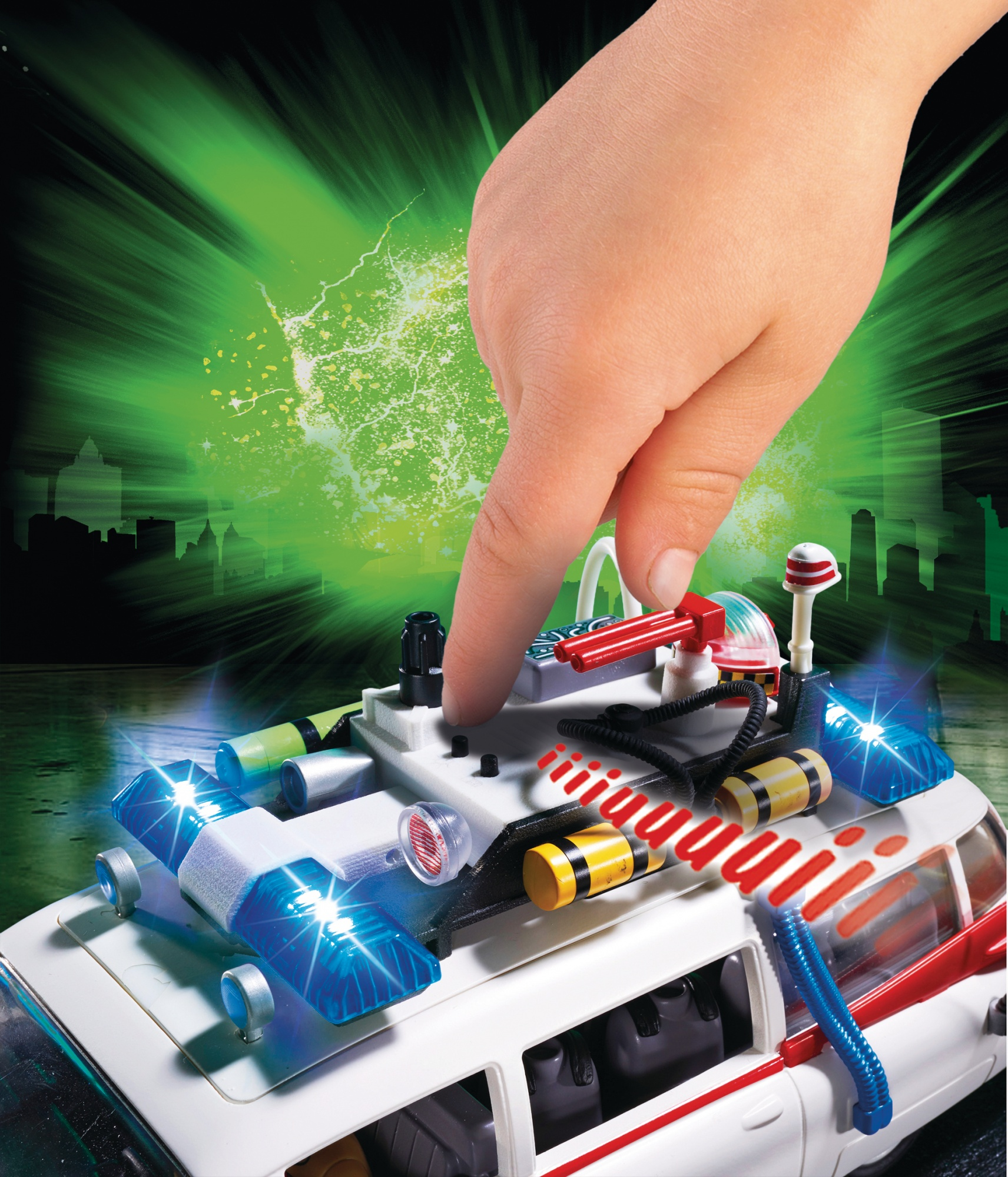 Dłoń wskazuje na górę białego samochodu-zabawki Ghostbusters z migającymi światłami. Zielone tło.