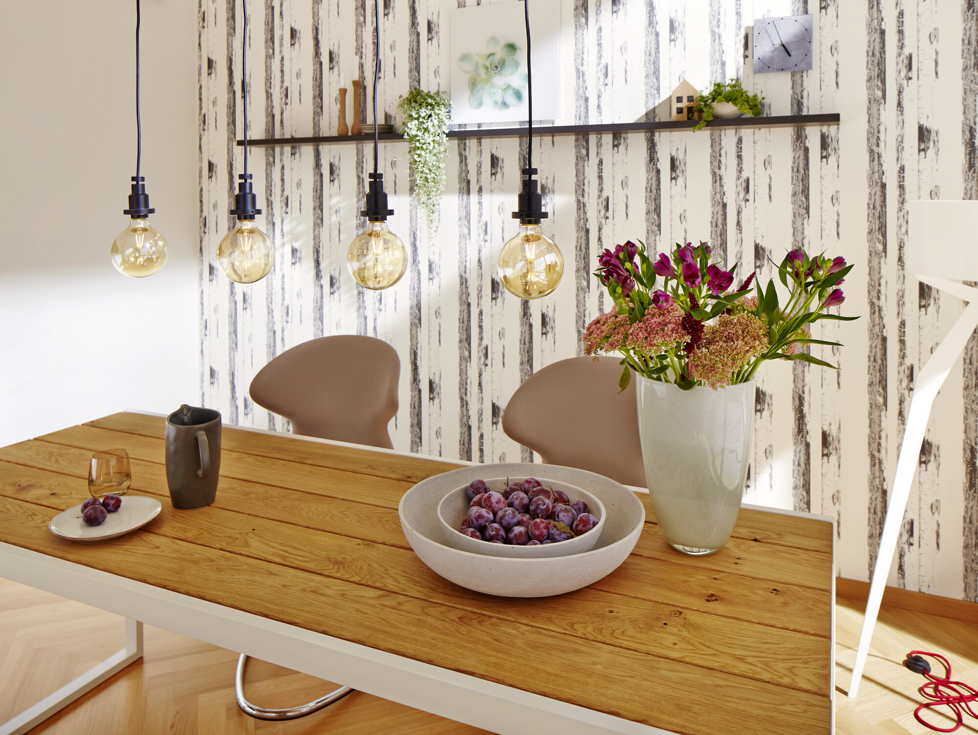Jadalnia z drewnianym stołem i krzesłami. Kwiaty i żarówki zwisające z sufitu.
