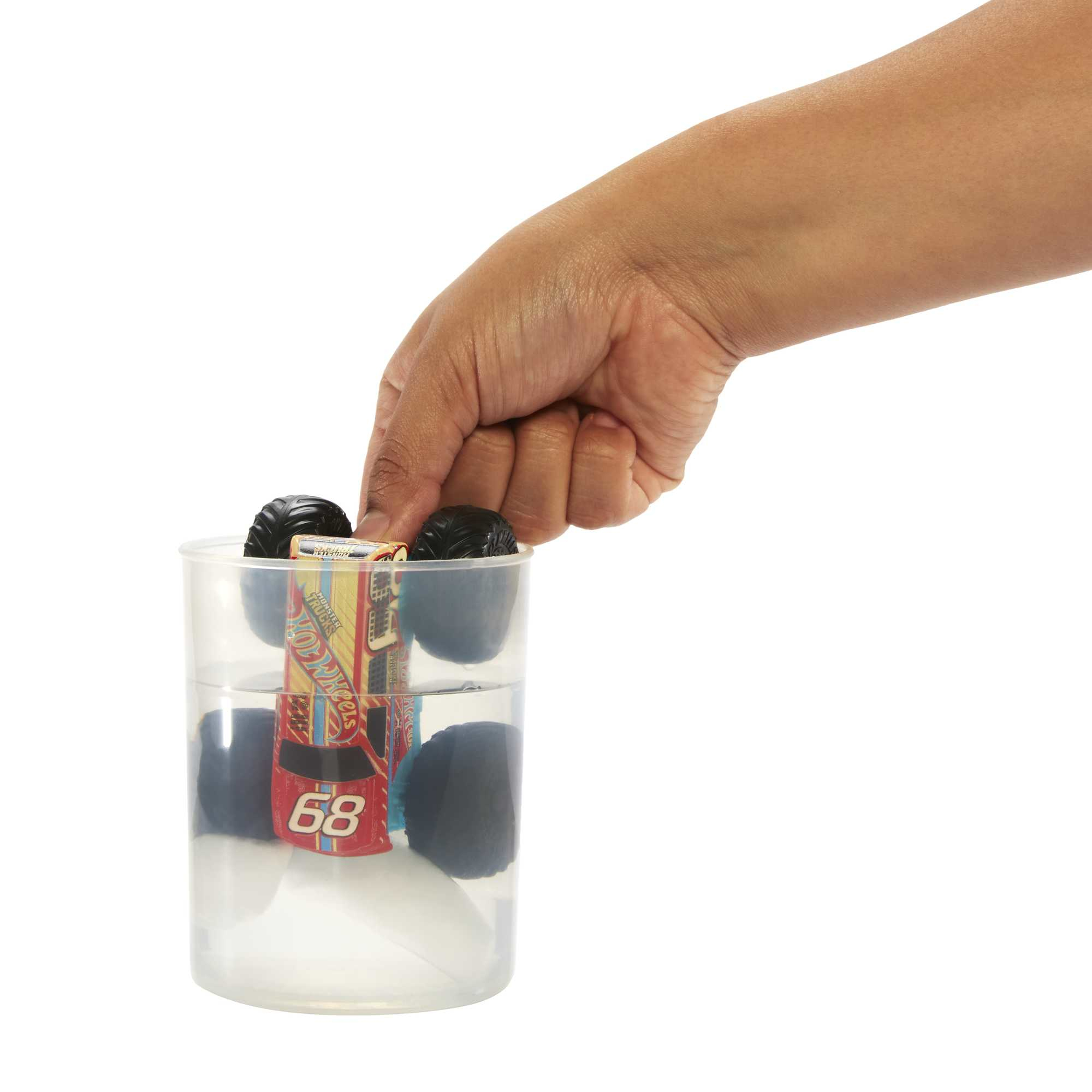 Ręka zanurzająca czerwono-niebieską ciężarówkę w wodzie. Używane jest przezroczyste szkło.