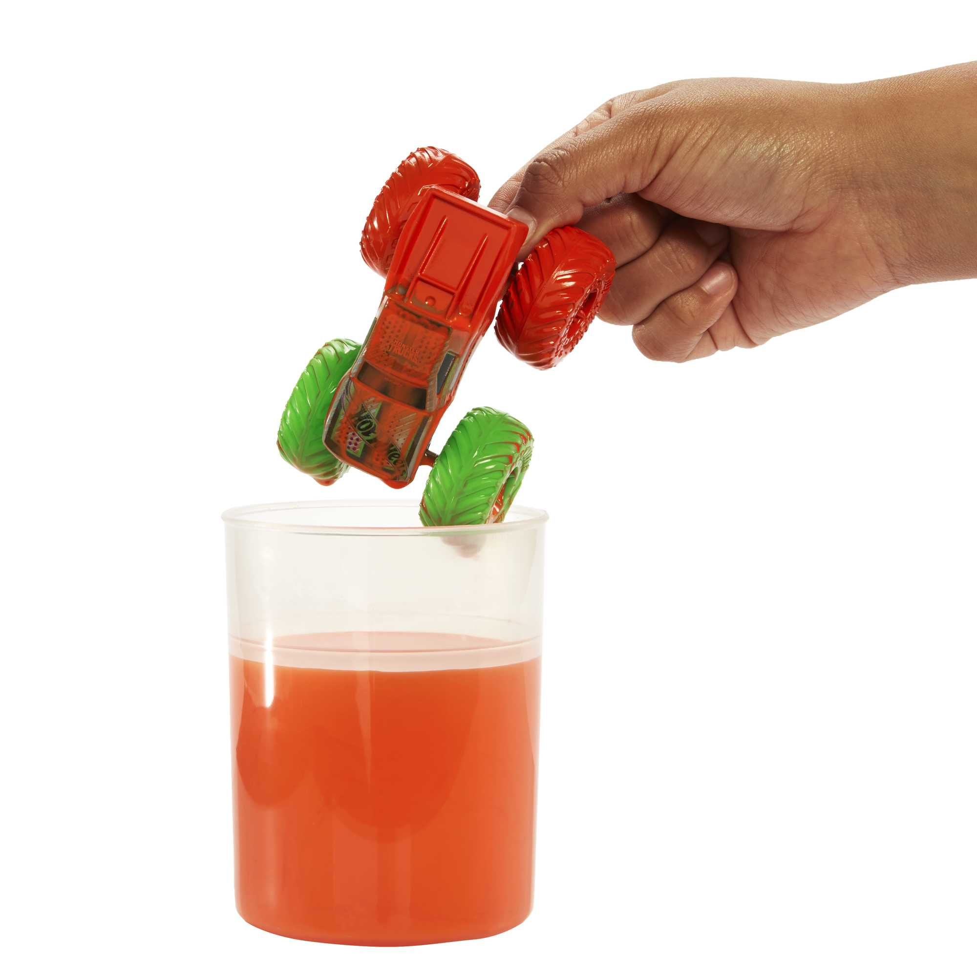 Czerwona zabawka ciężarówki potwora umieszczana w szklance z pomarańczowym płynem.