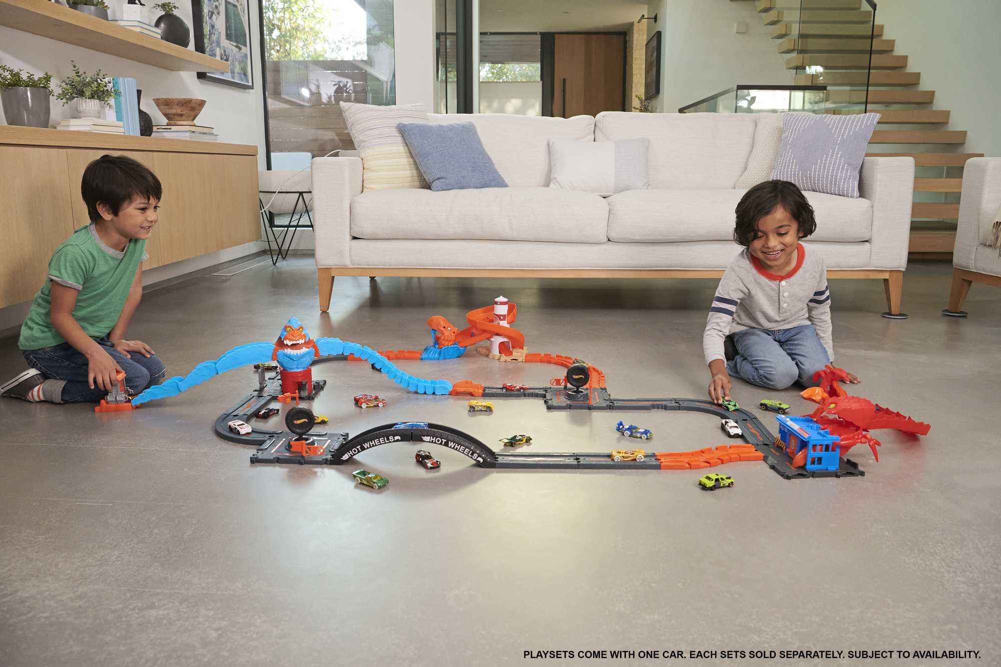 Zwei Jungen spielen mit einem Hot Wheels Streckenset. Autos und Strecke liegen auf dem Boden.
