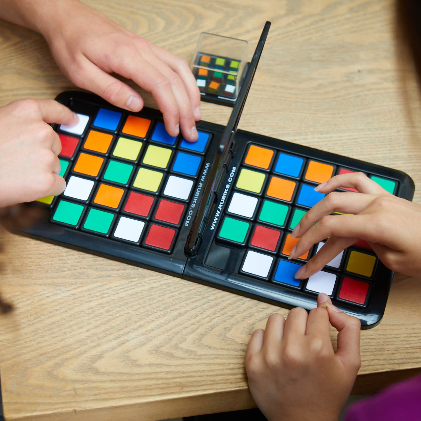 Dos personas jugando Rubik's Race, manos en el tablero con cuadrados de colores.