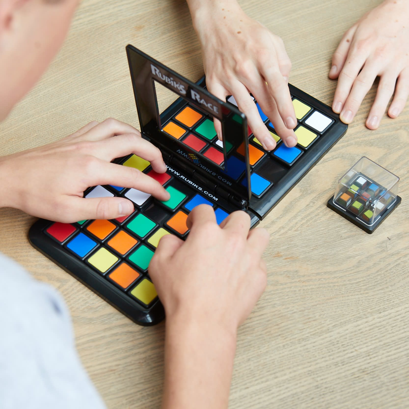 Dos personas jugando a Rubik's Race en una mesa de madera, con un pequeño Cubo de Rubik.